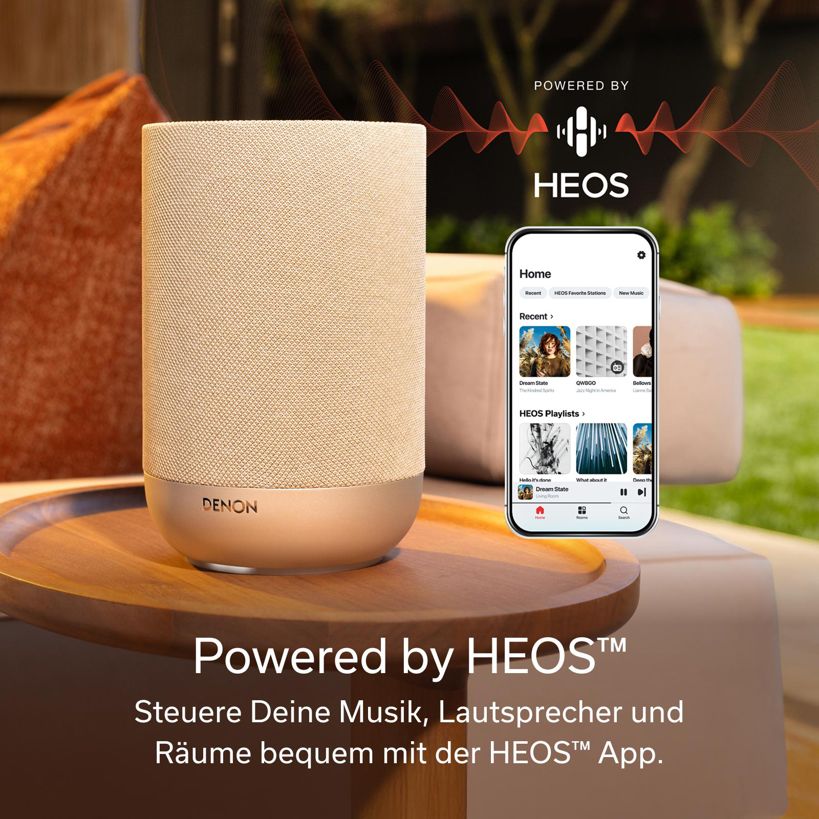Ein beige Lautsprecher von Denon steht auf einem Holzteller neben einem Smartphone.