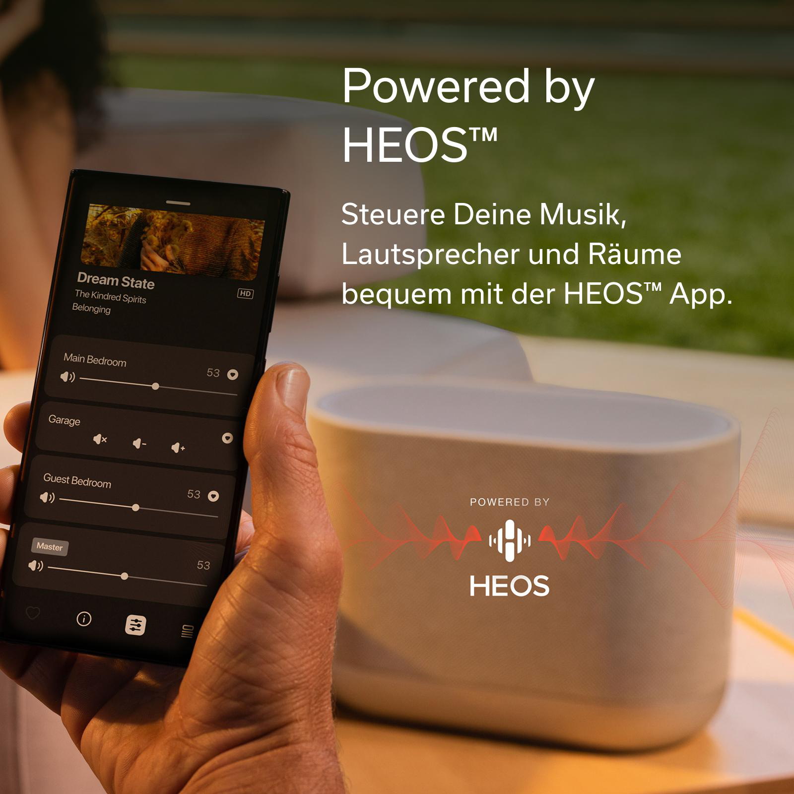 Ein Smartphone zeigt die HEOS App mit Musiksteuerung neben einem HEOS Lautsprecher.