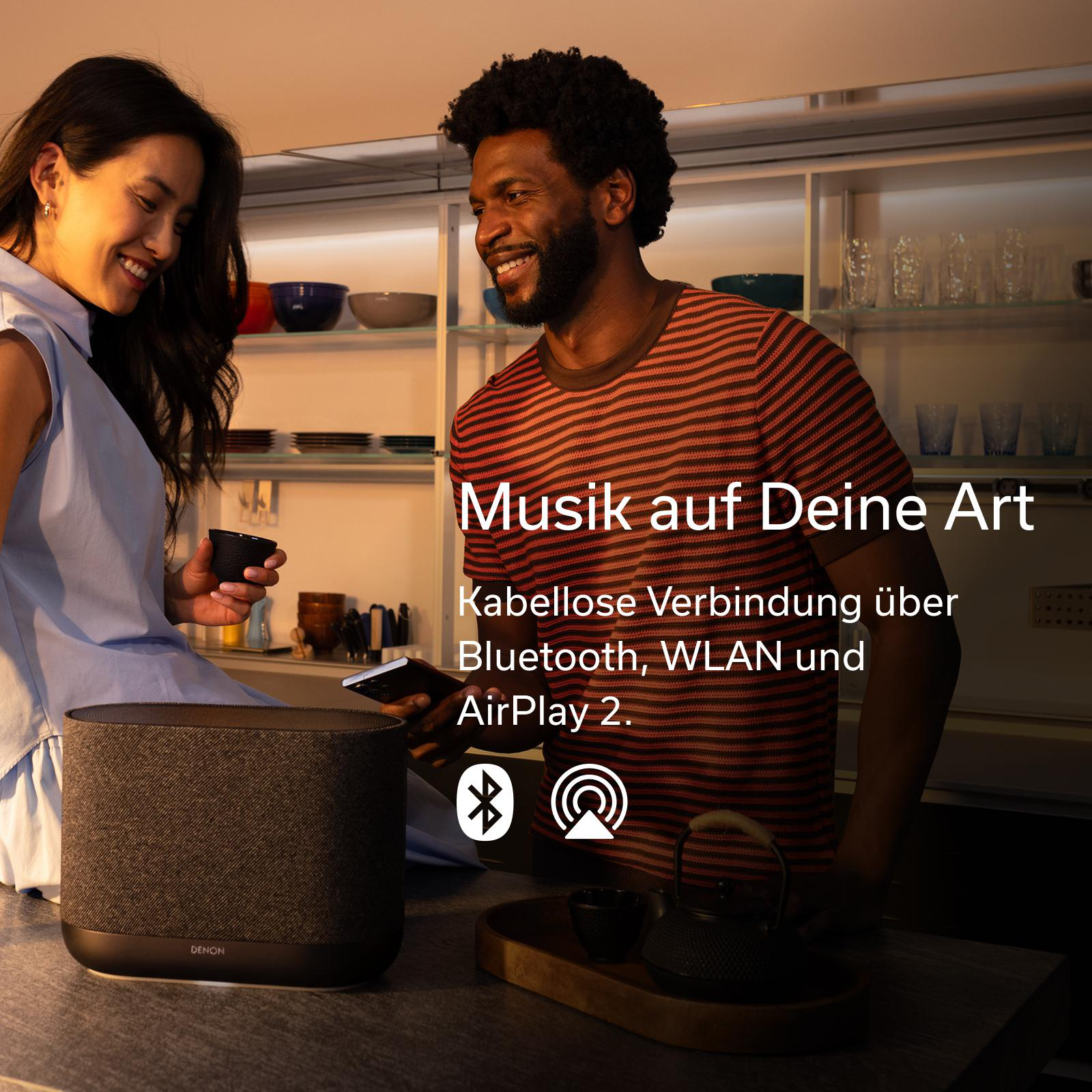 Mann und Frau in Küche mit Denon Lautsprecher. Musik kabellos über Bluetooth, WLAN, AirPlay 2.