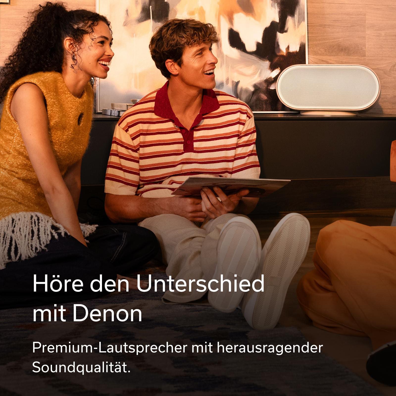 Zwei junge Leute sitzen auf dem Boden vor einem Lautsprecher und einem Gemälde.