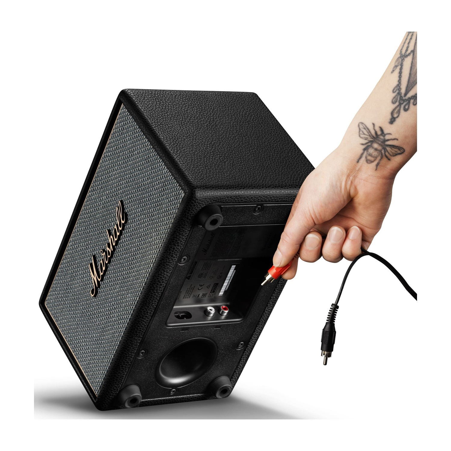 Una mano con tatuaggio di ape inserisce cavo RCA rosso in altoparlante Marshall nero.