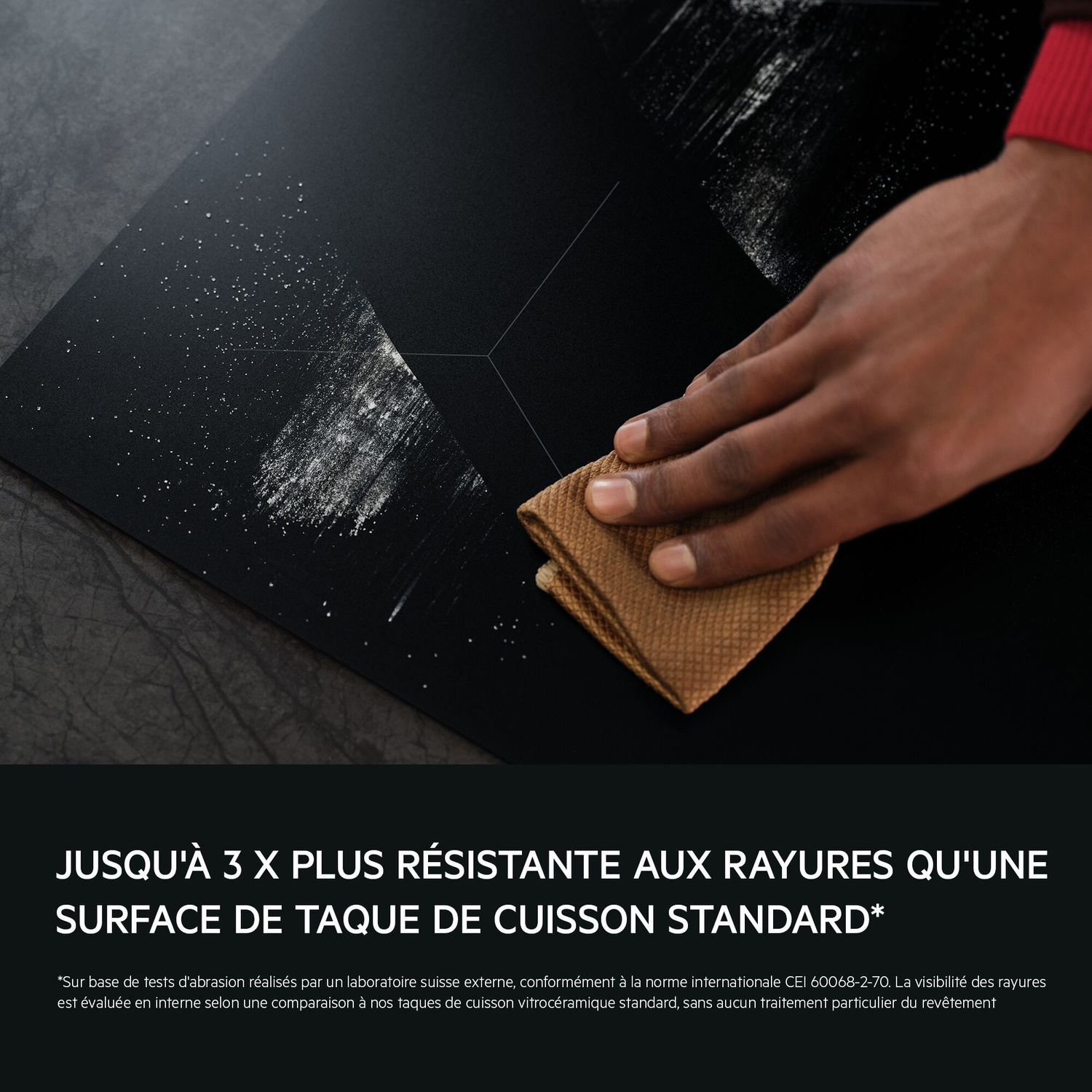 Une main nettoie une plaque de cuisson noire avec un tissu marron.