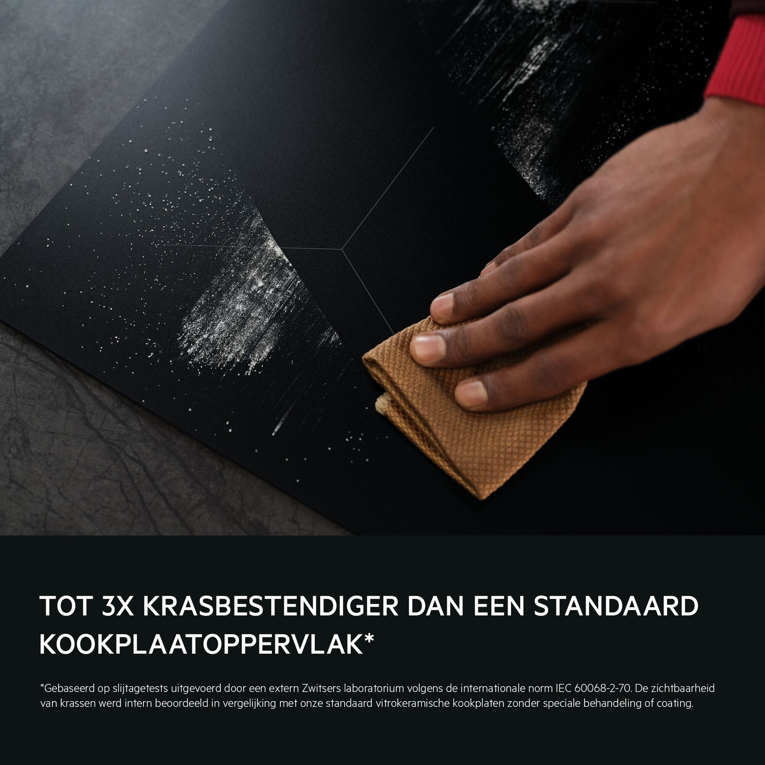 Een hand reinigt een zwart kookplaat oppervlak met een bruine doek.