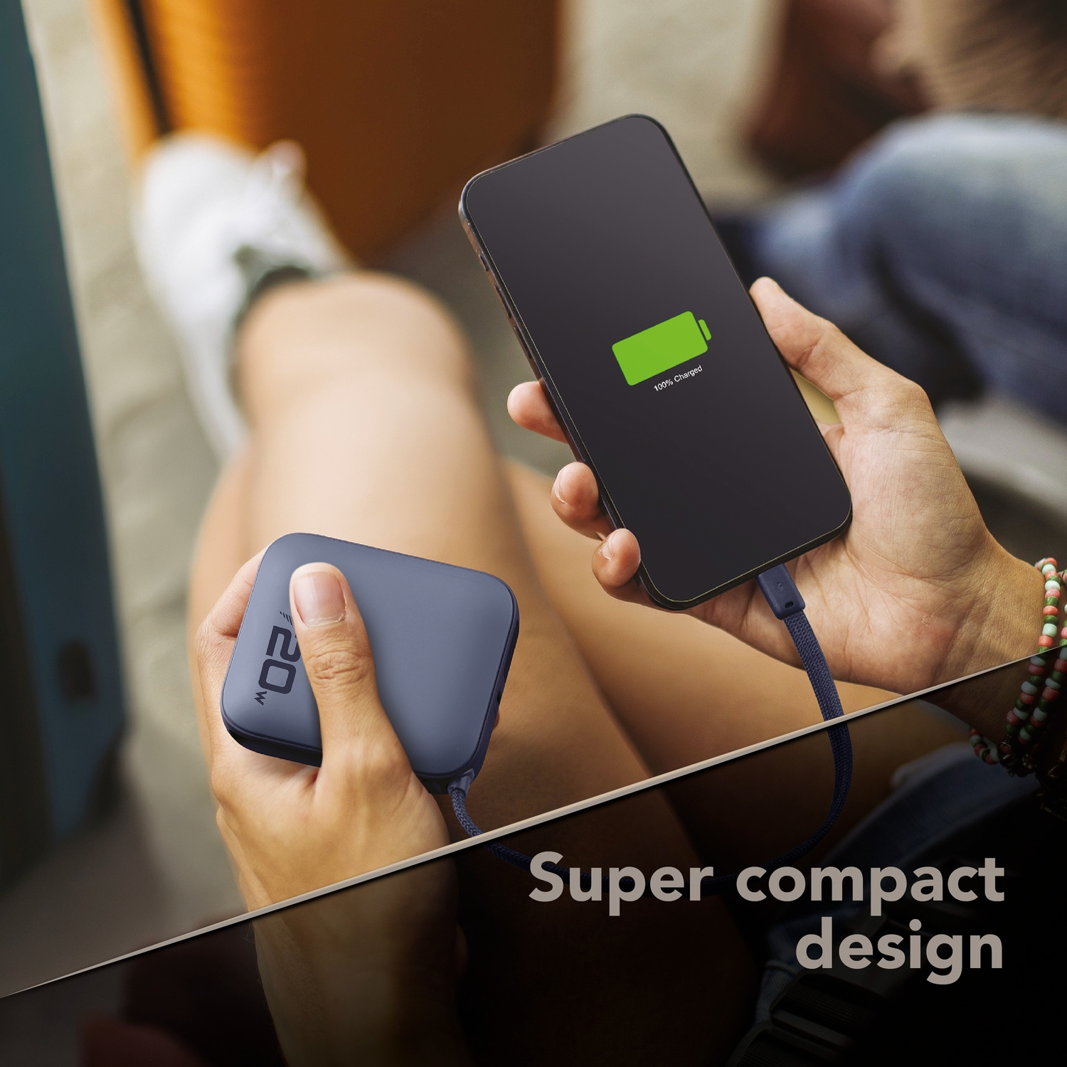 Una persona carica un telefono con un power bank blu. Display 100%.