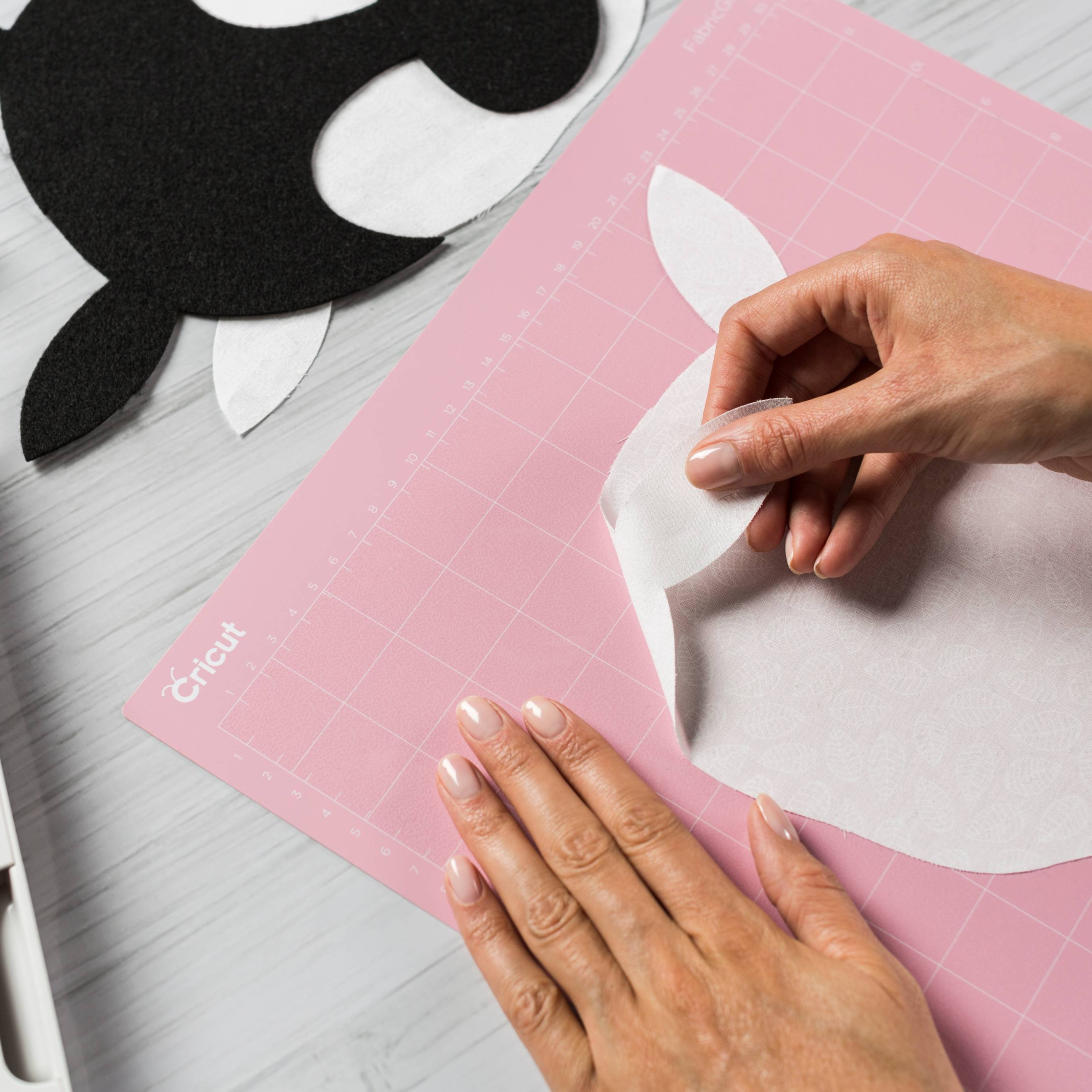 Eller, pembe bir Cricut kesim matına beyaz bir kumaş parçası yerleştiriyor.