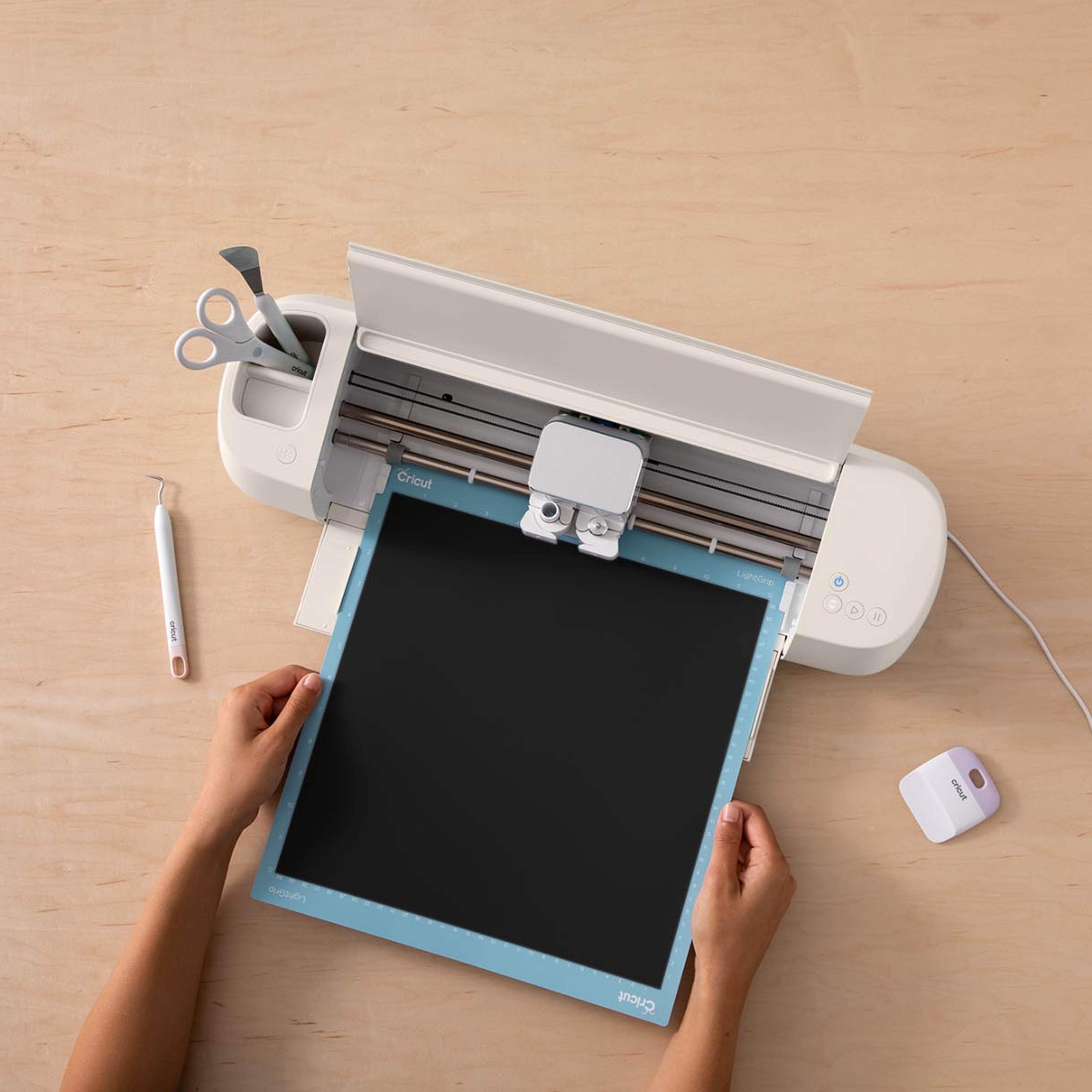Beyaz bir Cricut kesme makinesi ahşap bir masada aletlerle duruyor.