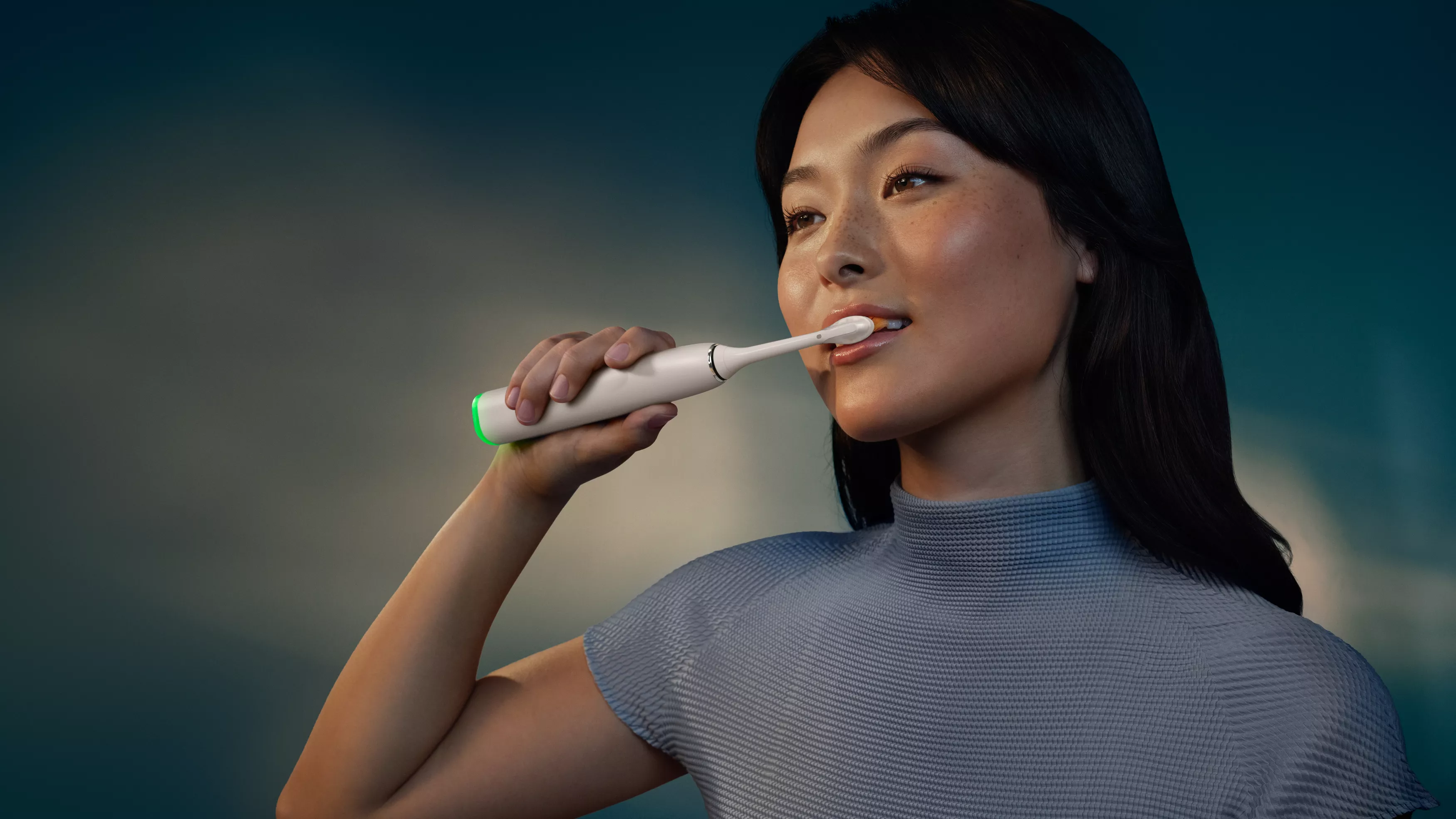 Une femme se brosse les dents avec une brosse électrique.