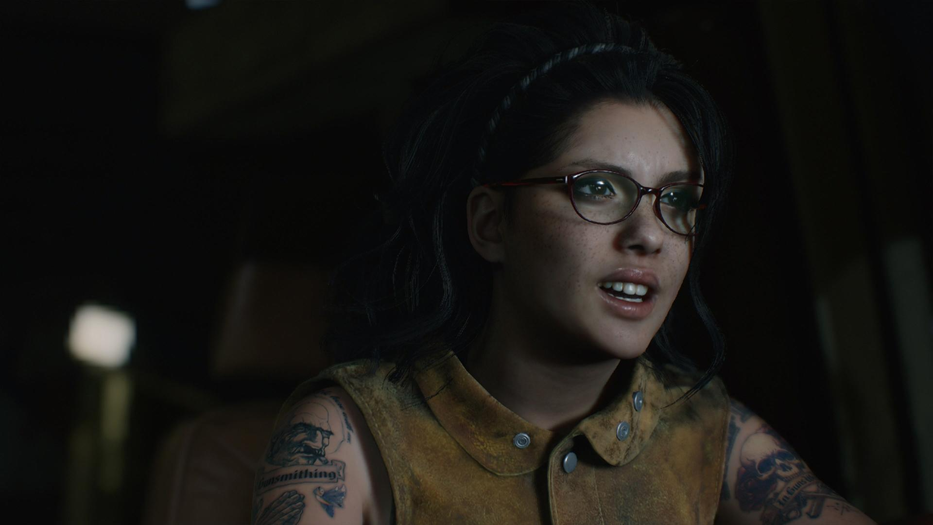 Nahaufnahme einer jungen Frau mit Brille, Sommersprossen und Tattoos. Sie trägt eine braune Weste.