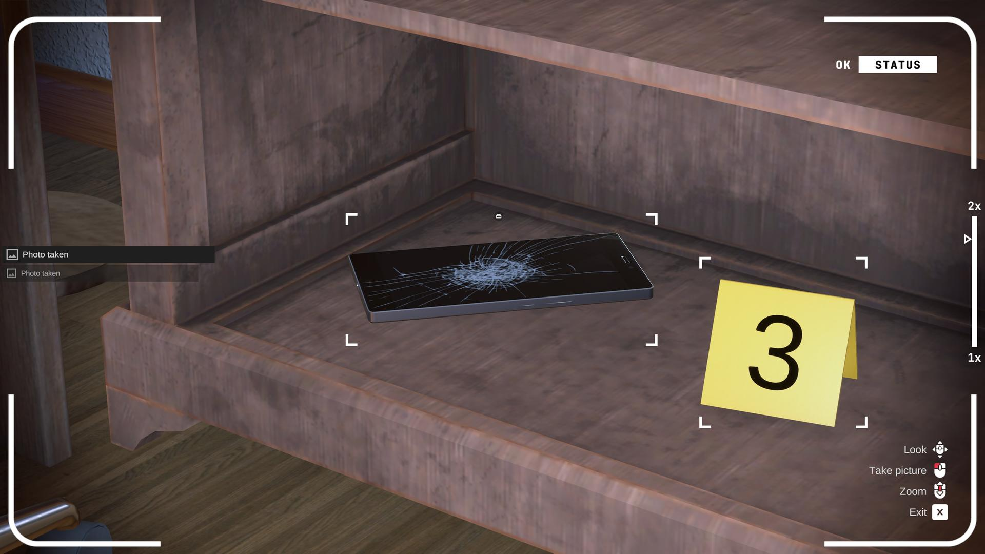 Ein kaputtes Smartphone liegt auf einem Regal neben einem gelben Hinweisschild mit der Zahl 3.