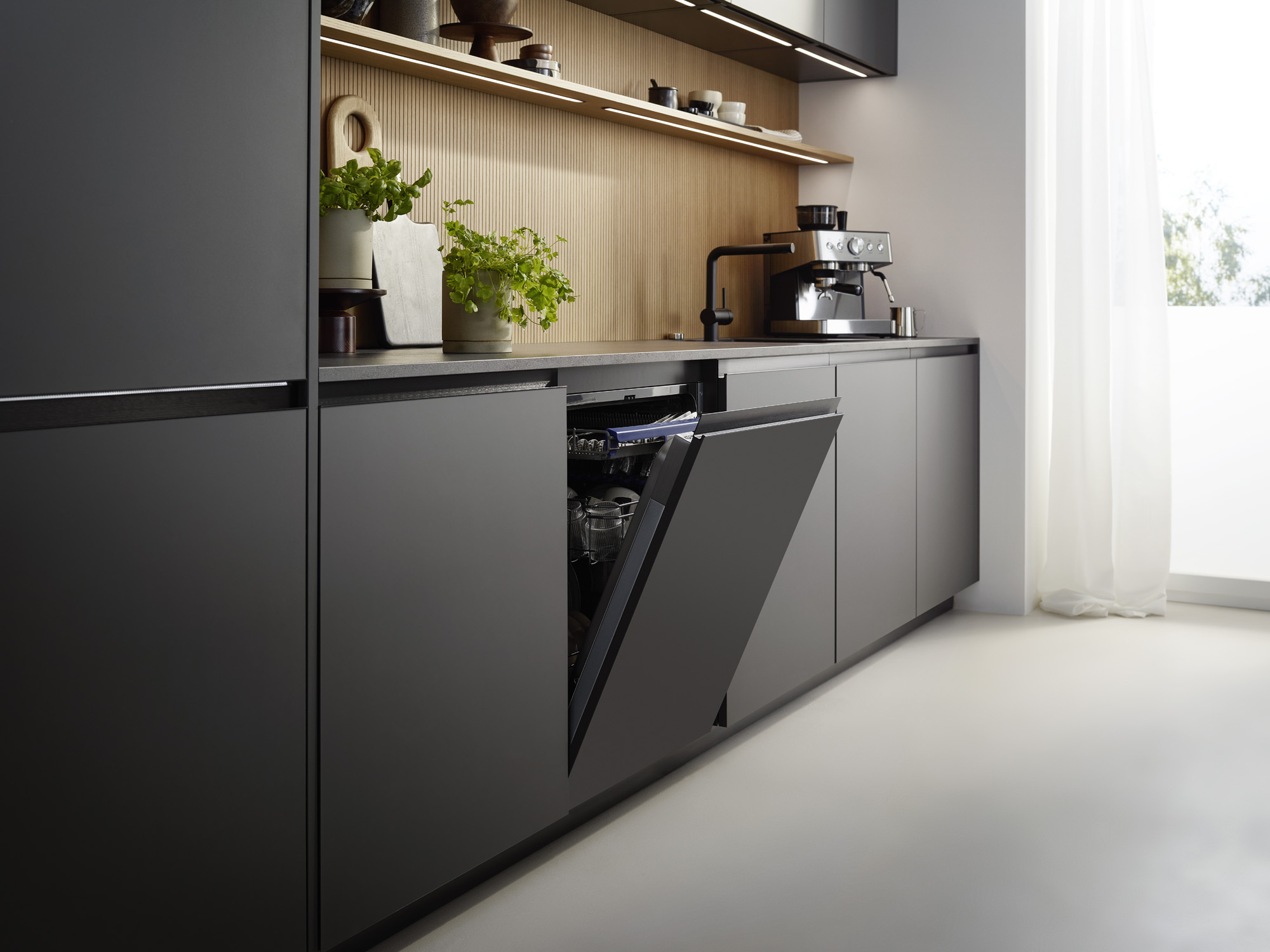 Moderne Küche mit geöffnetem Geschirrspüler, Espressomaschine und Pflanzen.