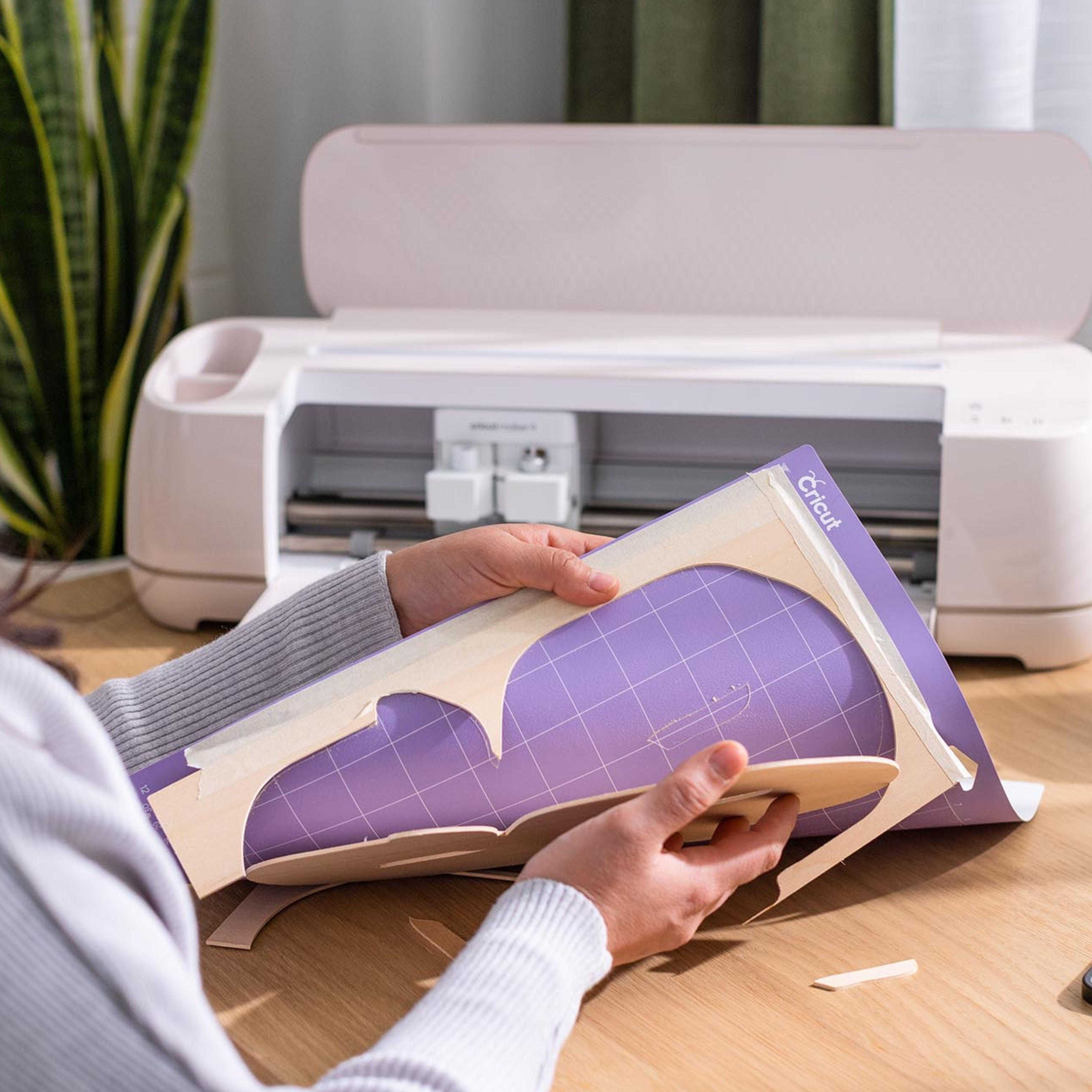 Eller Cricut makinesinin yanındaki mor kesme matından ahşap şekli soyuyor.