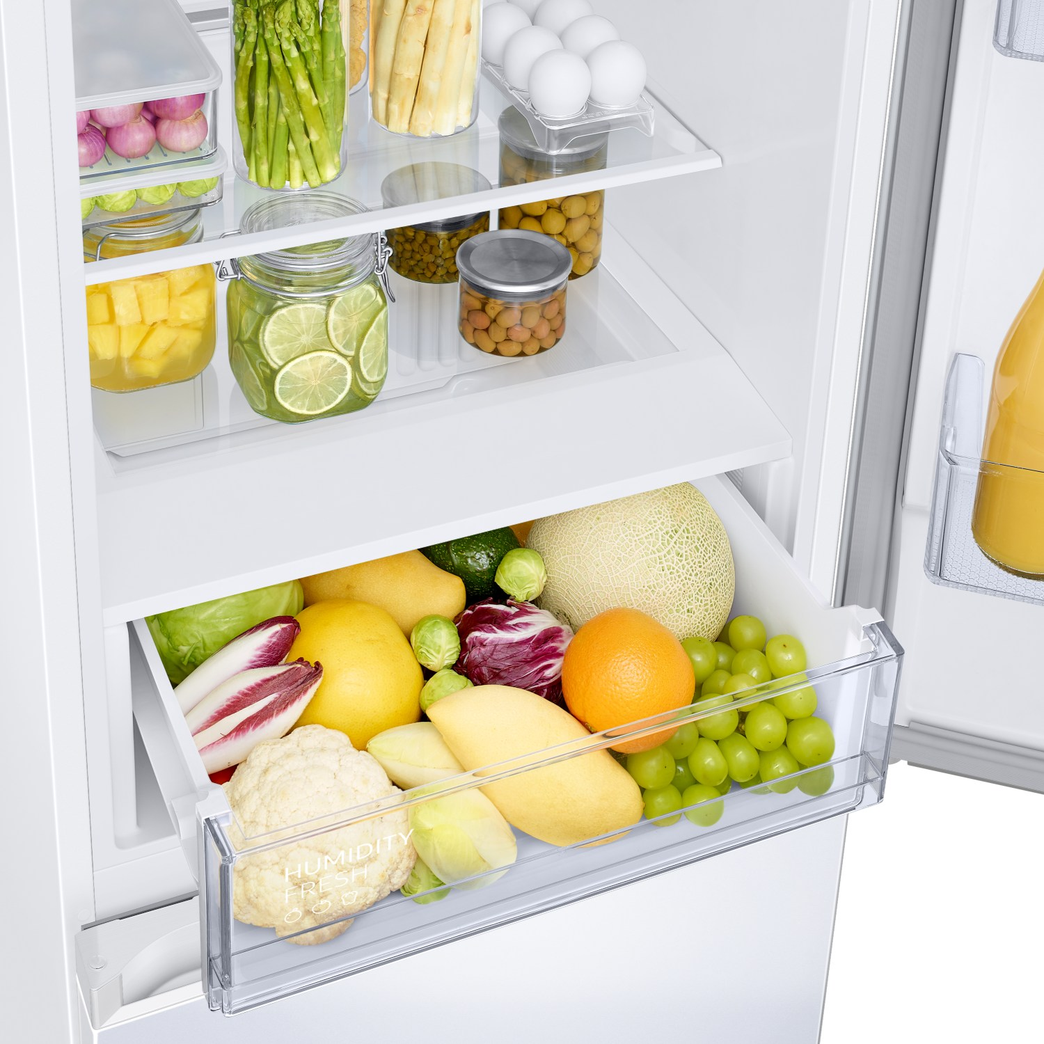 Un refrigerador blanco abierto con varias frutas frescas, verduras y artículos en frascos en estantes y en un cajón 'Humidity Fresh'.