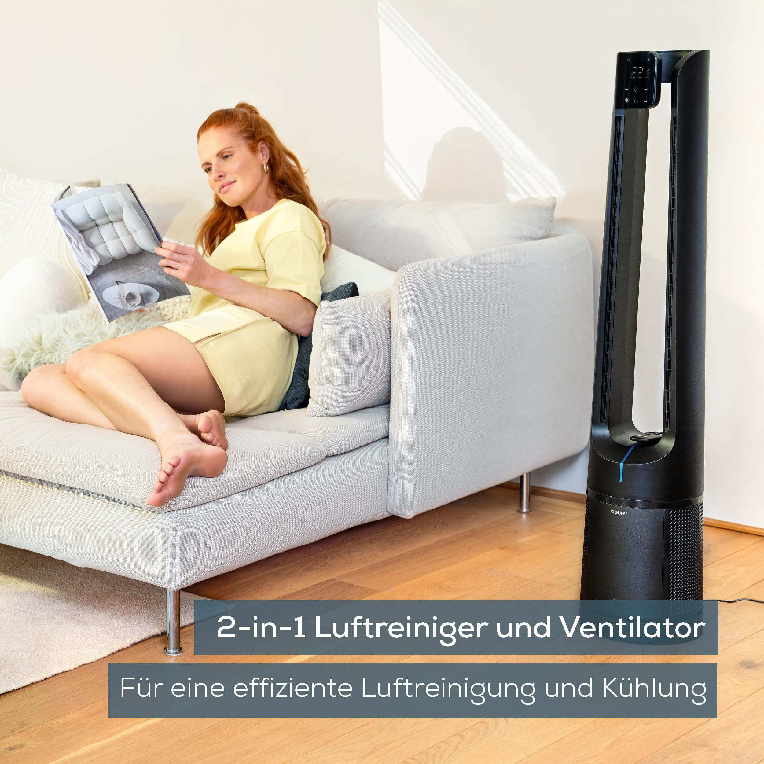 Eine Frau liest auf einem hellgrauen Sofa neben einem schwarzen Luftreiniger und Ventilator mit Digitalanzeige, die 22 anzeigt.