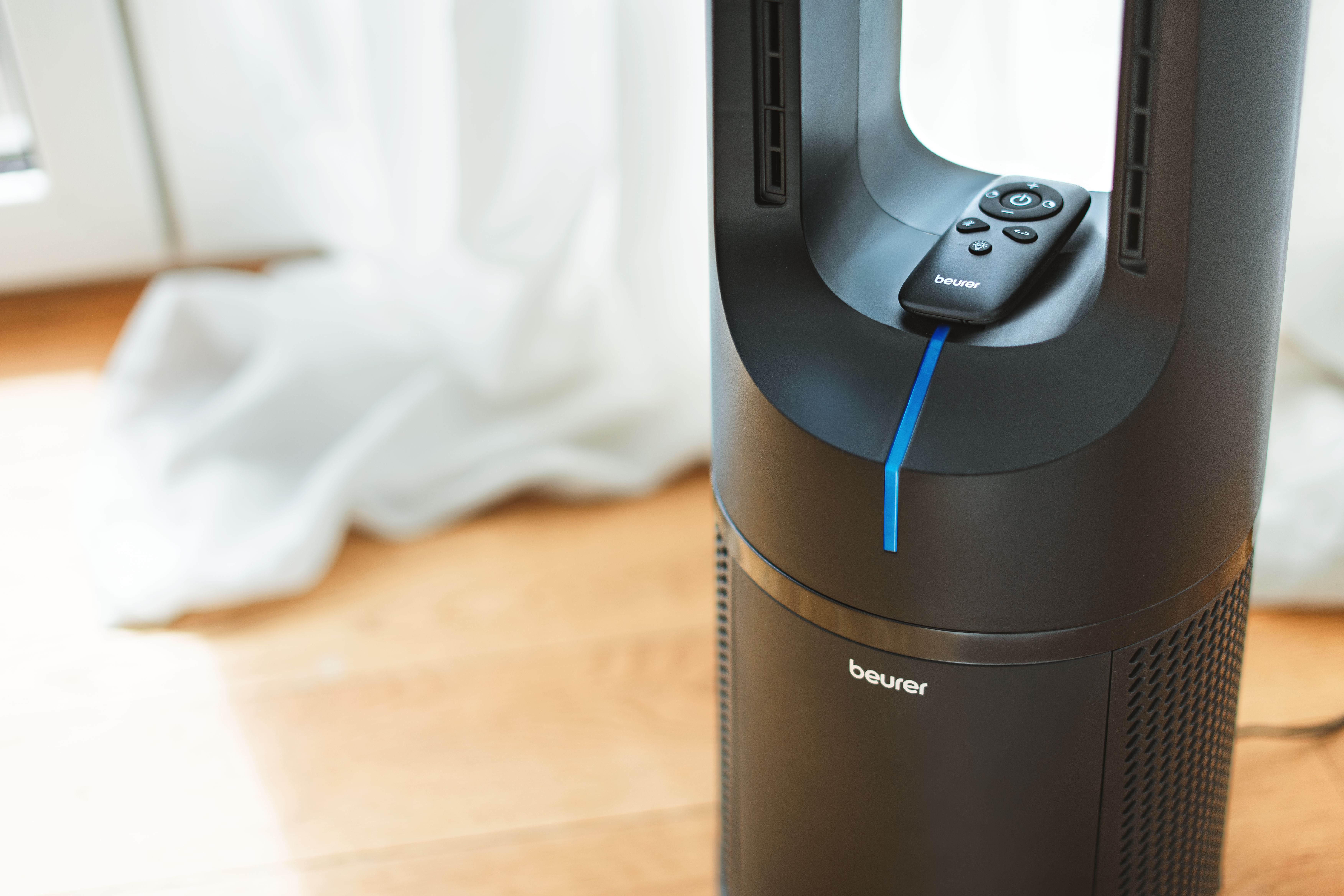 Ein schwarzer Turmventilator mit Fernbedienung auf dem Boden.