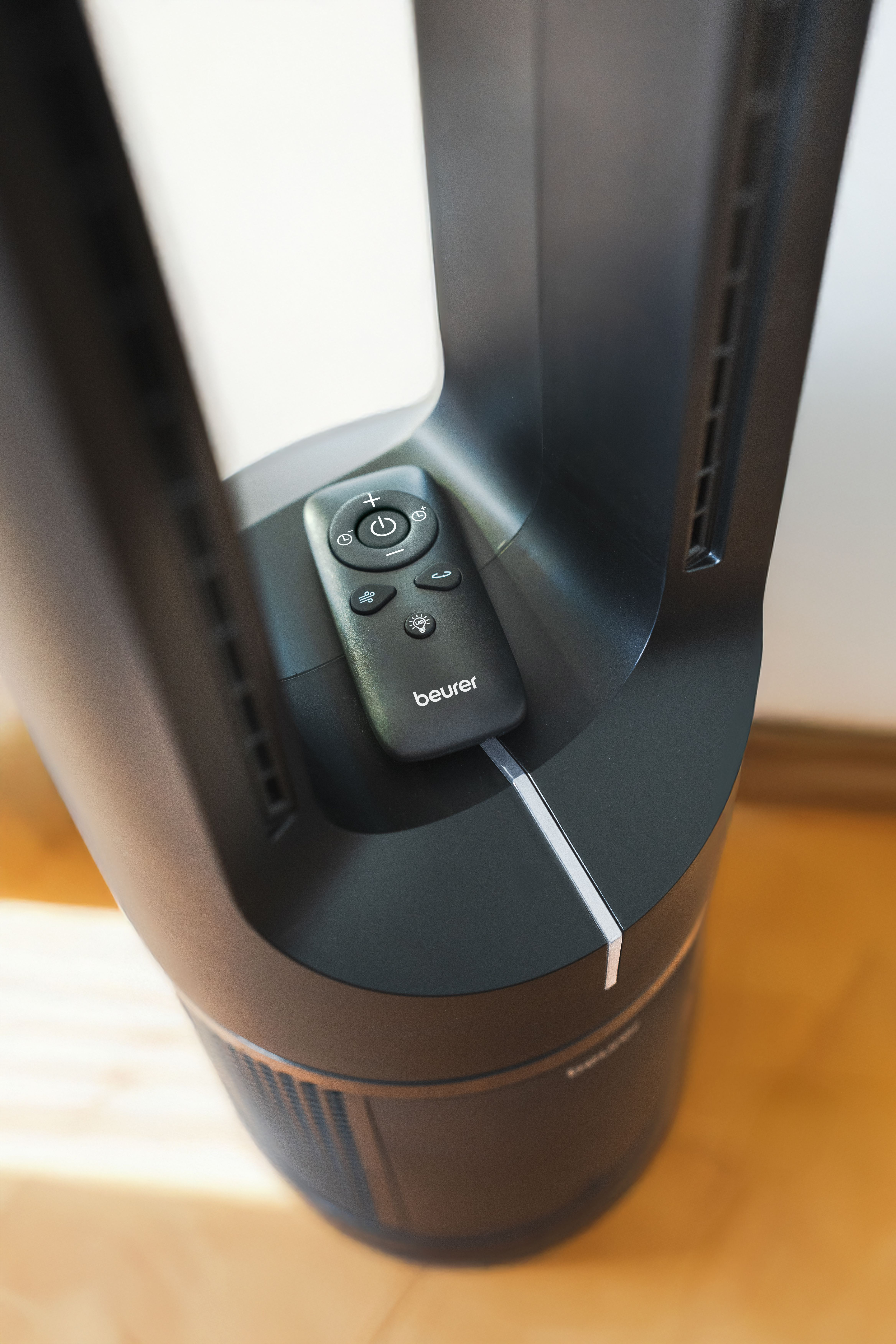 Eine schwarze Fernbedienung liegt in einer Vertiefung eines schwarzen Turmventilators.
