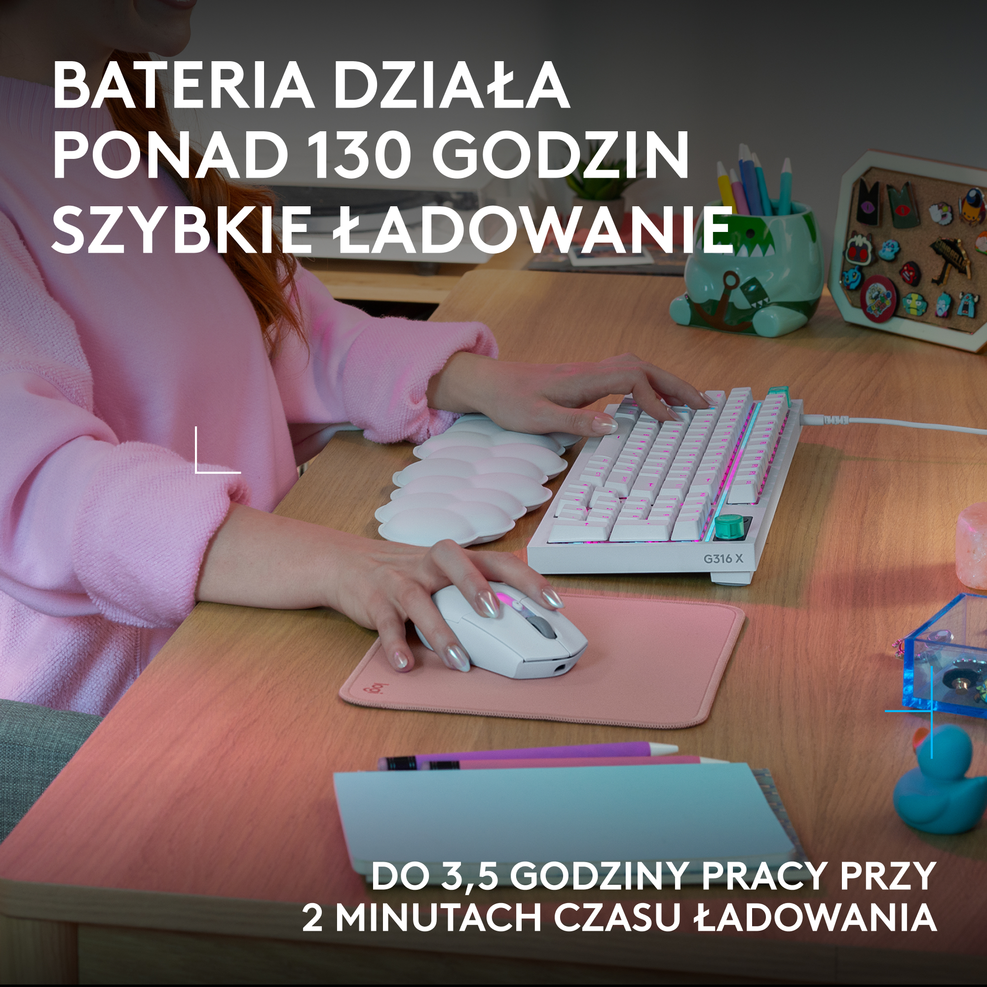 Osoba pisze na białej klawiaturze, mysz na różowej macie. Biurko z akcesoriami.
