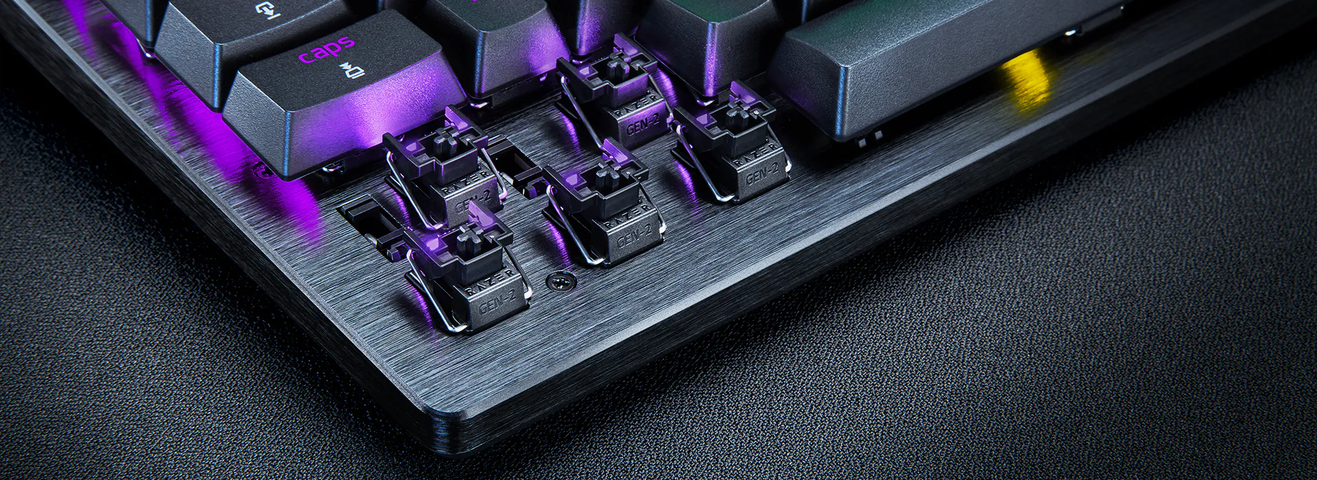 Primo piano di una tastiera meccanica con retroilluminazione viola e switch visibili.