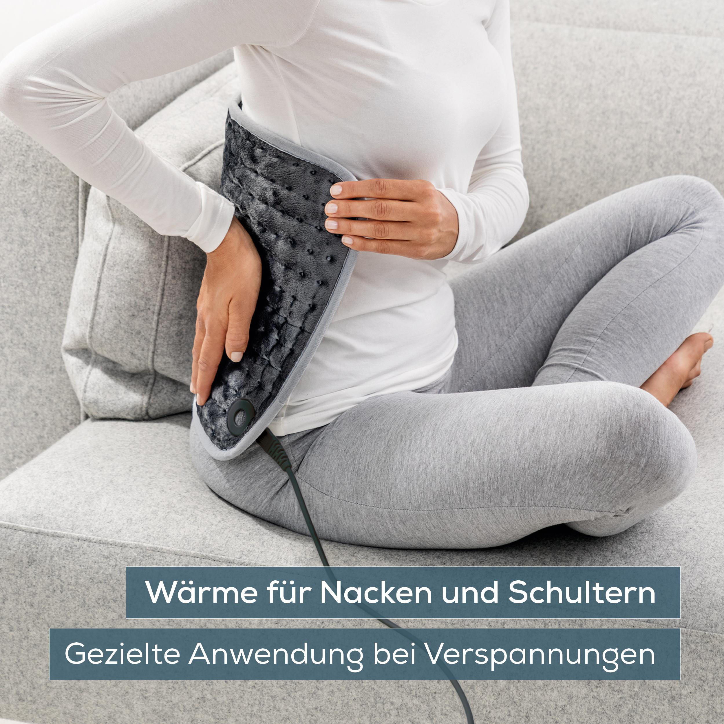 Eine Person mit einem Heizkissen auf dem Schoß auf einem Sofa.