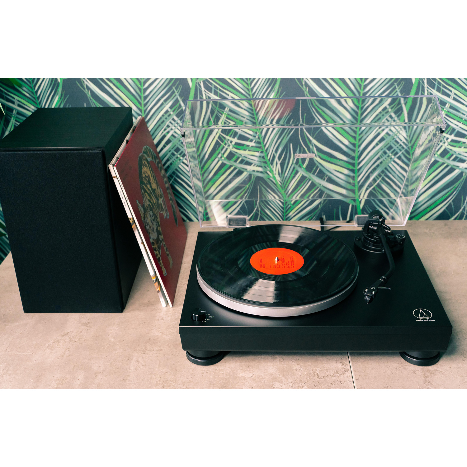 Giradischi nero con vinile e altoparlante, su sfondo di carta da parati con foglie di palma.