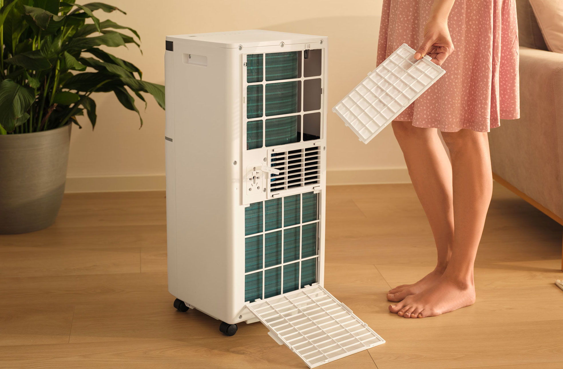 Osoba trzyma biały filtr przed klimatyzatorem z otwartymi żaluzjami.