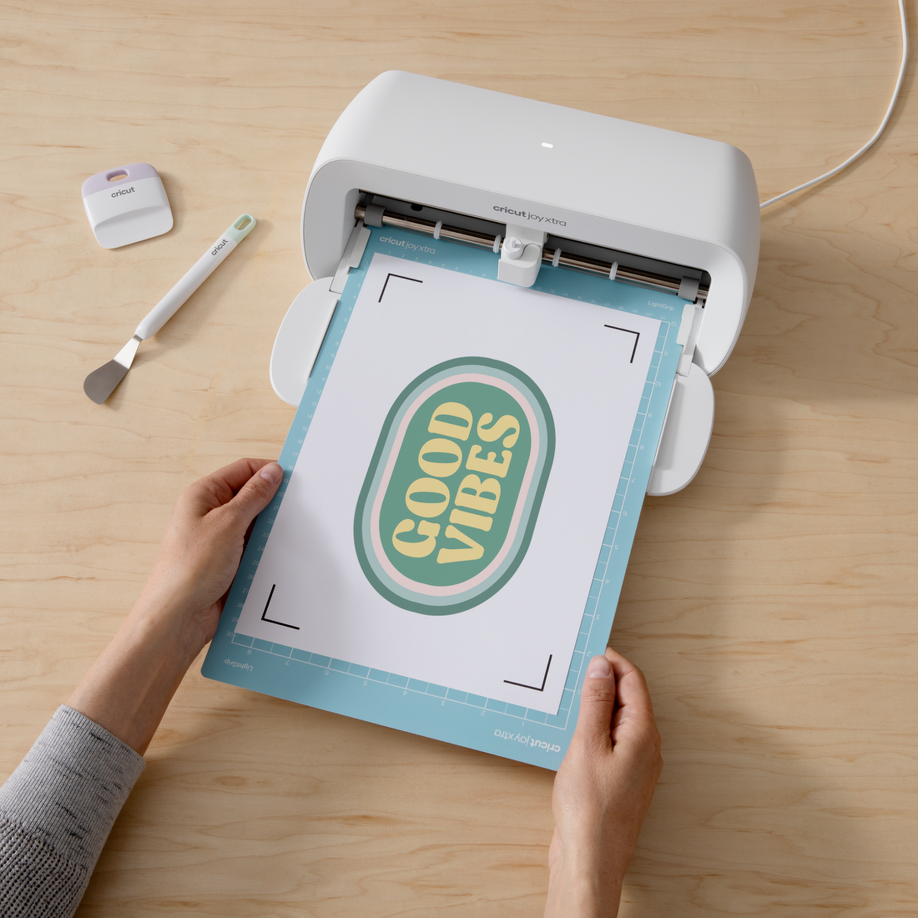 Eller "GOOD VIBES" yazılı kağıdı Cricut Joy Xtra makinesine yerleştiriyor.