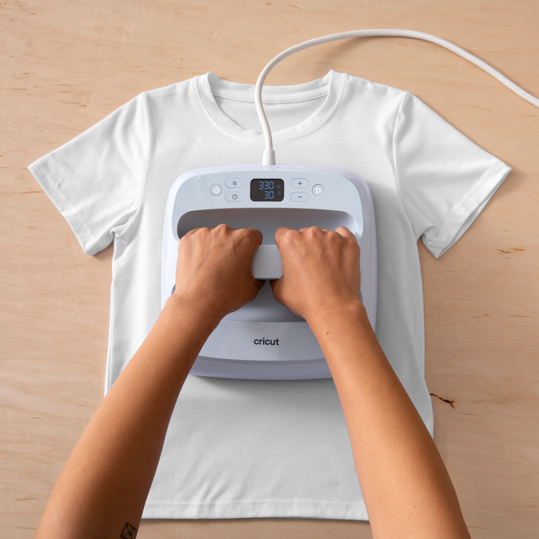 Ahşap masa üzerinde Cricut presi ile beyaz tişörtü tutan eller.