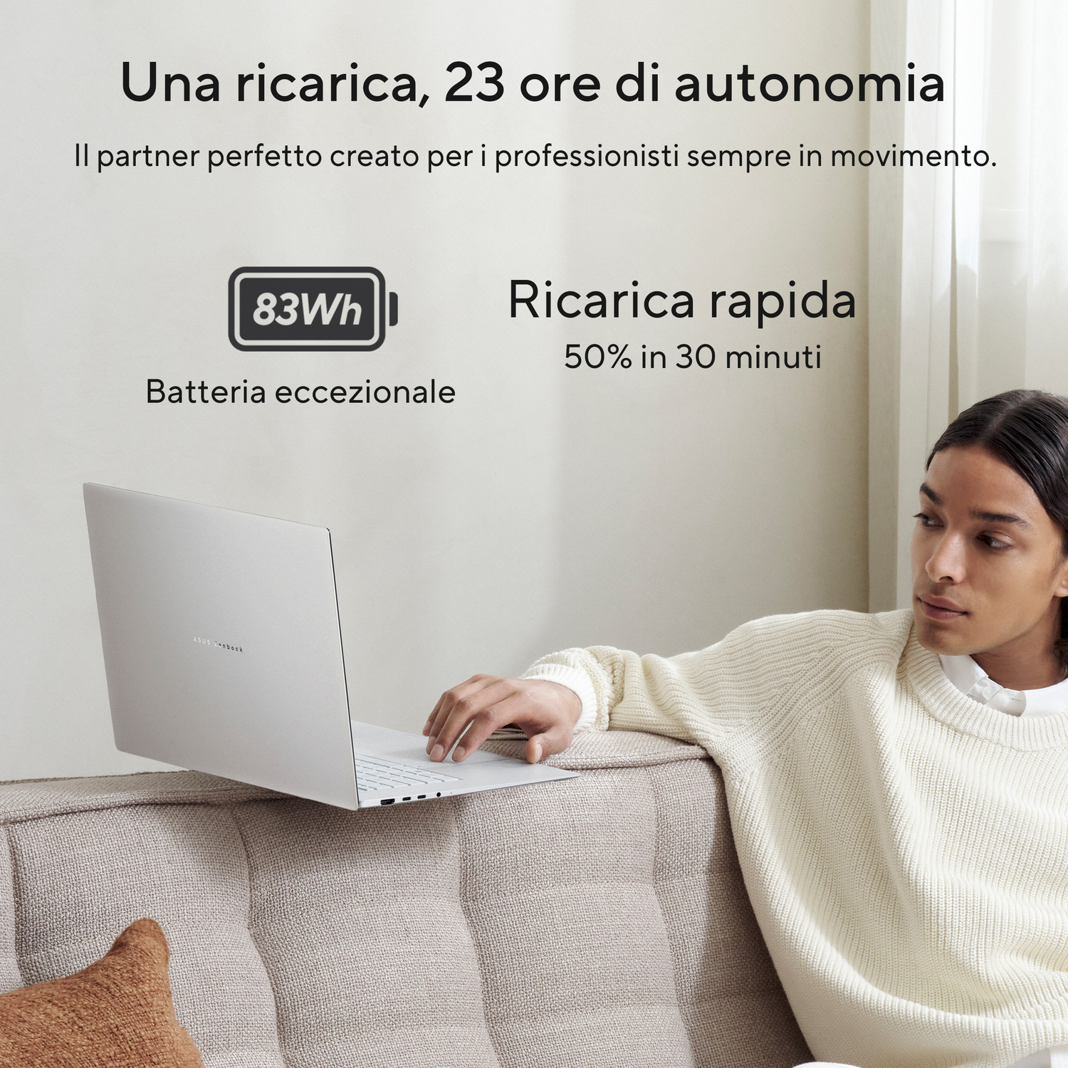 Una persona seduta su un divano con un laptop argentato che mostra batteria da 83 Wh e informazioni di ricarica rapida.