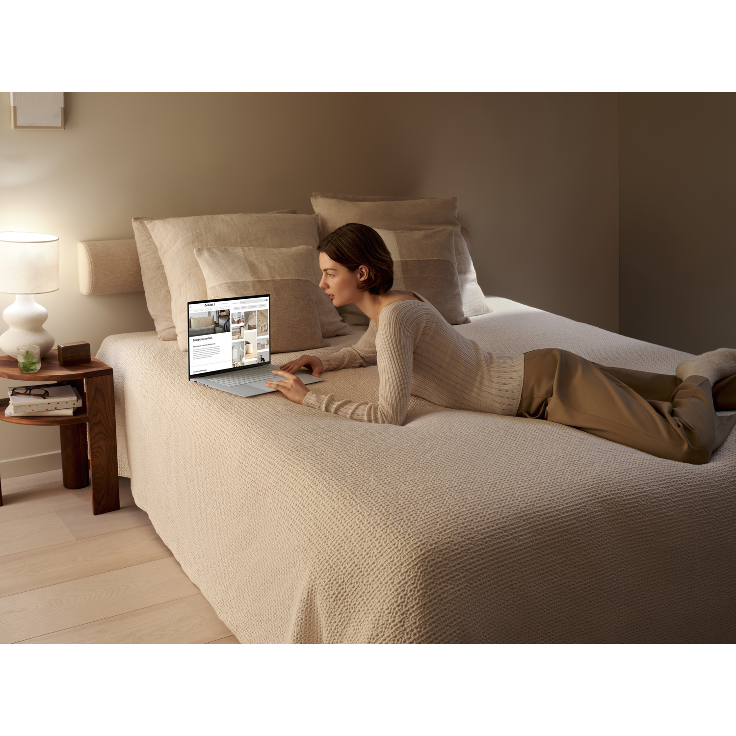 Una donna è sdraiata su un letto usando un laptop. Un comodino con una lampada è accanto a lei.
