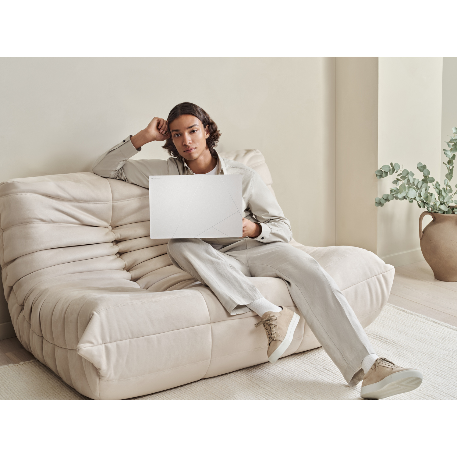 Un uomo seduto su un divano beige tiene in mano un laptop bianco.