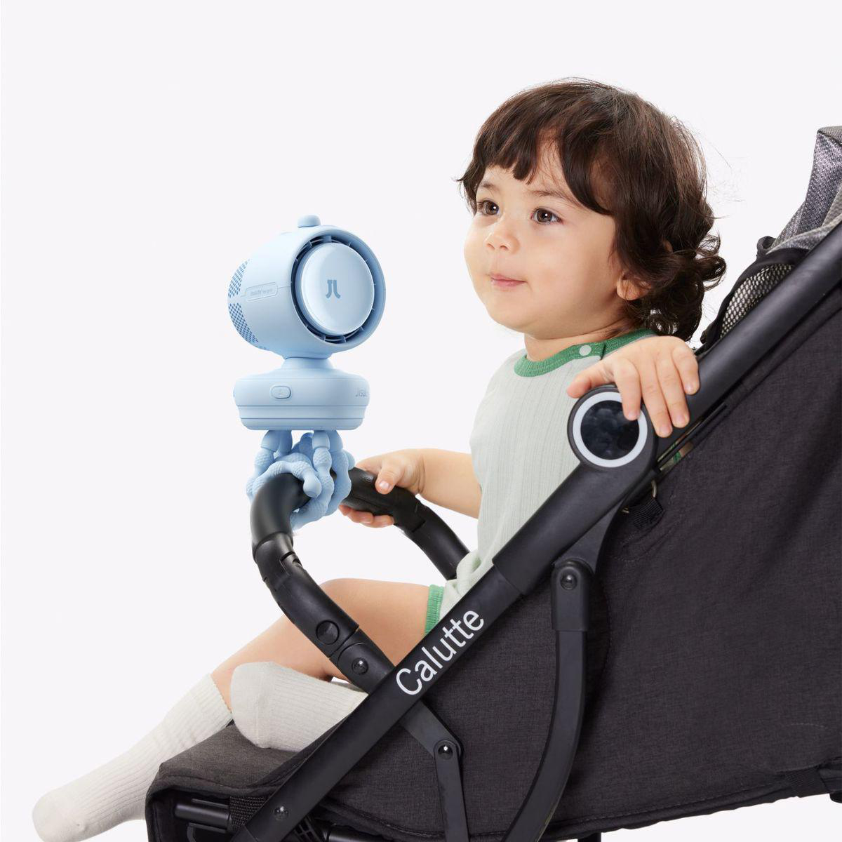 Kleines Kind sitzt im Kinderwagen mit einem blauen Ventilator daneben.