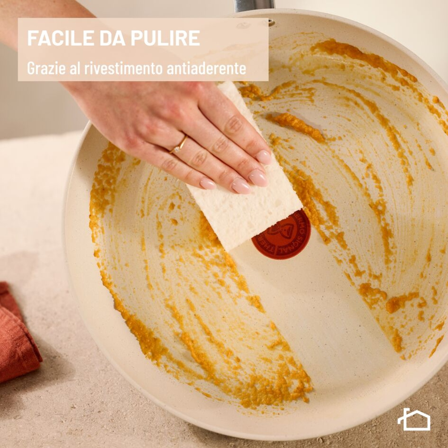 Una mano pulisce una padella con residui gialli usando una spugna.