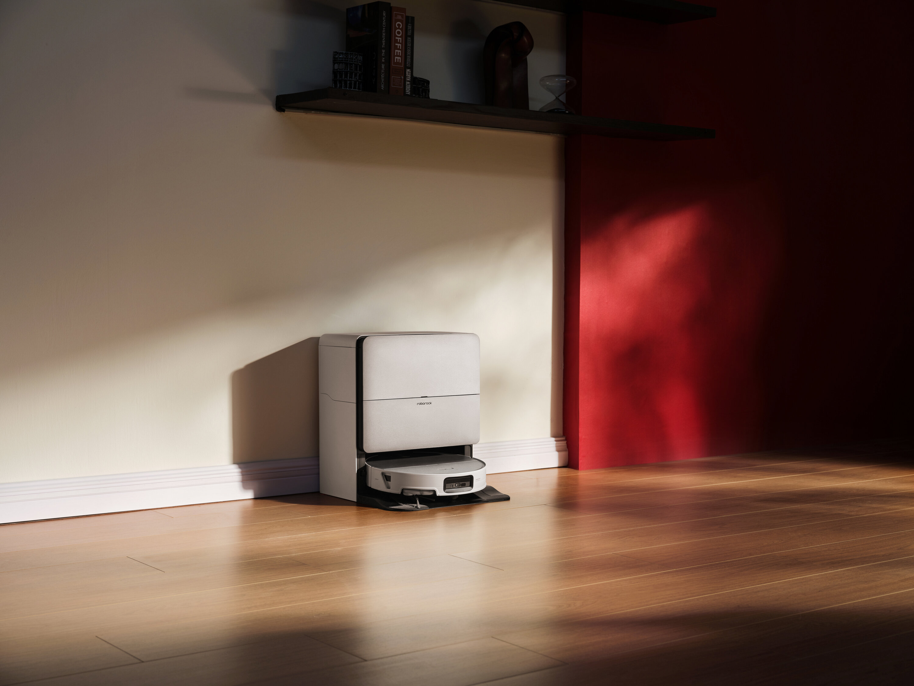 Biały robot sprzątający stoi na stacji ładującej przy ścianie.