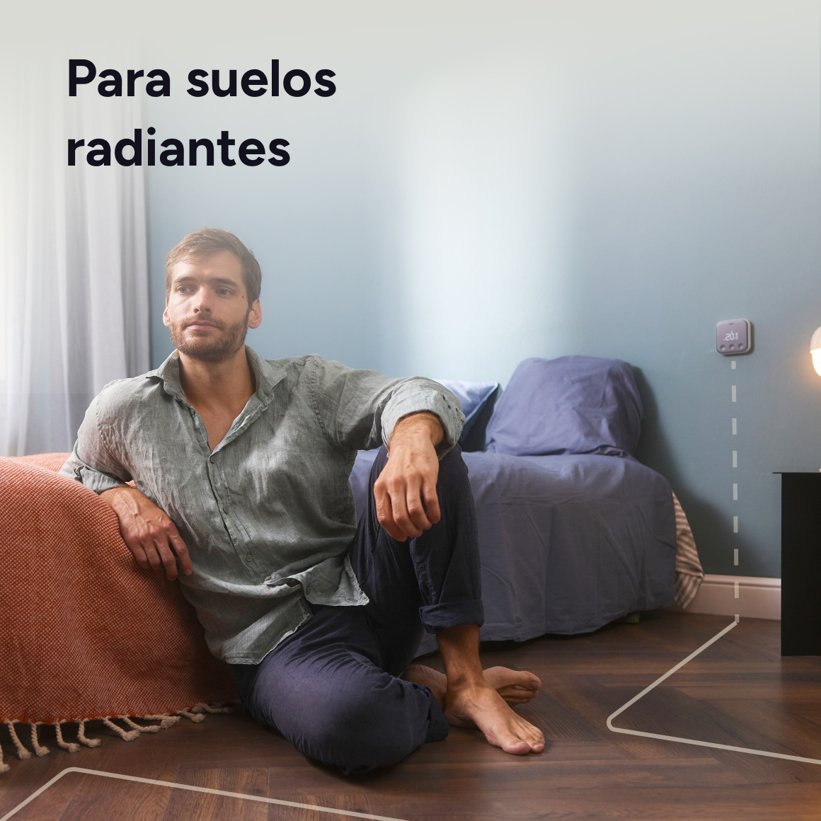 Hombre sentado en el suelo junto a una cama. Termostato en la pared.