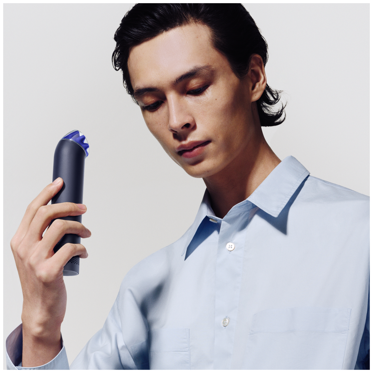 Man in light blue shirt holds dark device with blue tip.