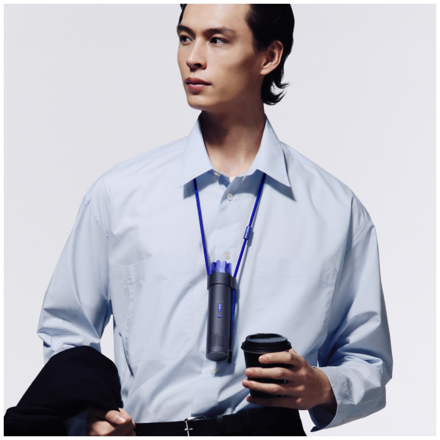 A man in a light blue shirt wears a necklace with a device and holds a coffee cup.