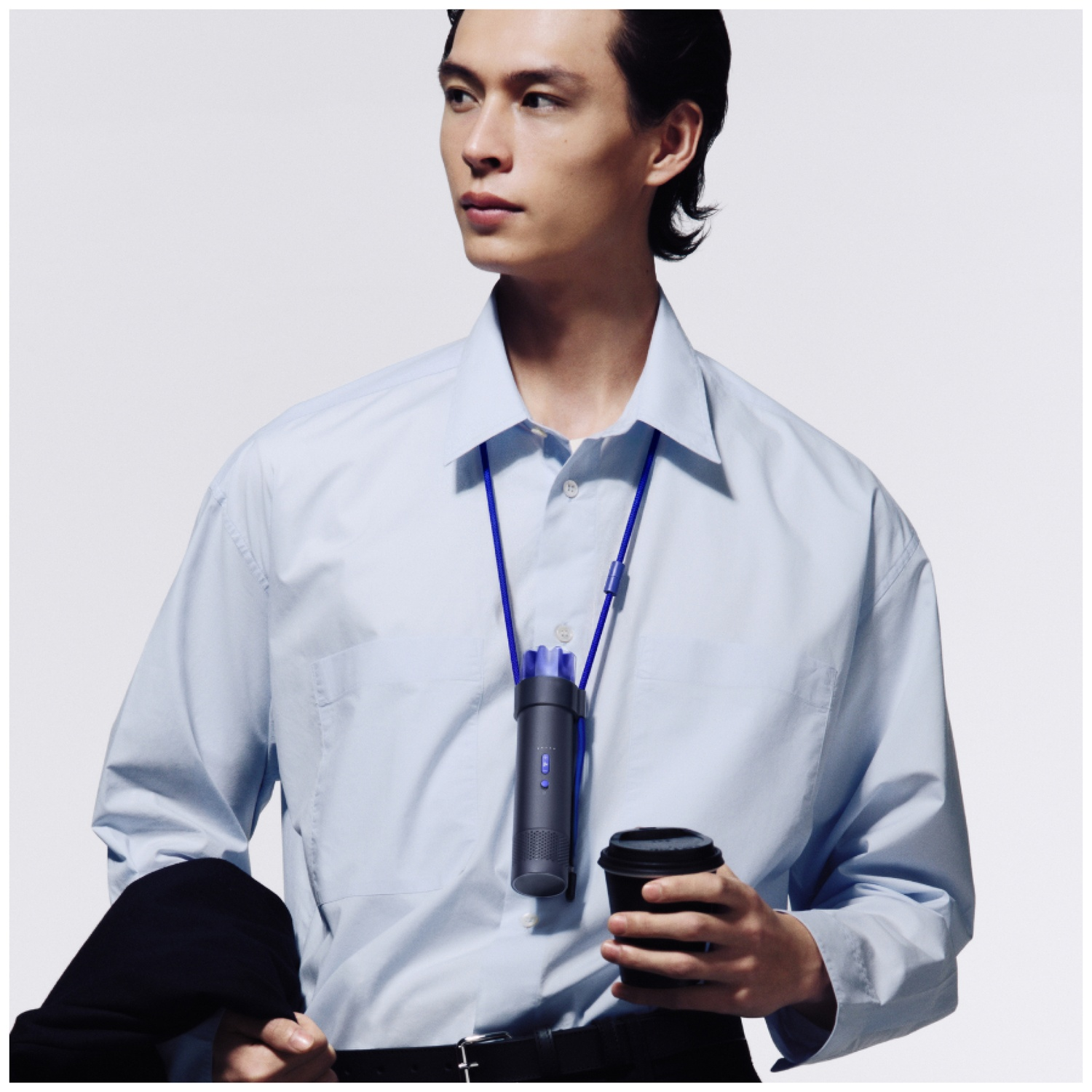 A man in a light blue shirt holds a coffee cup and a black jacket.