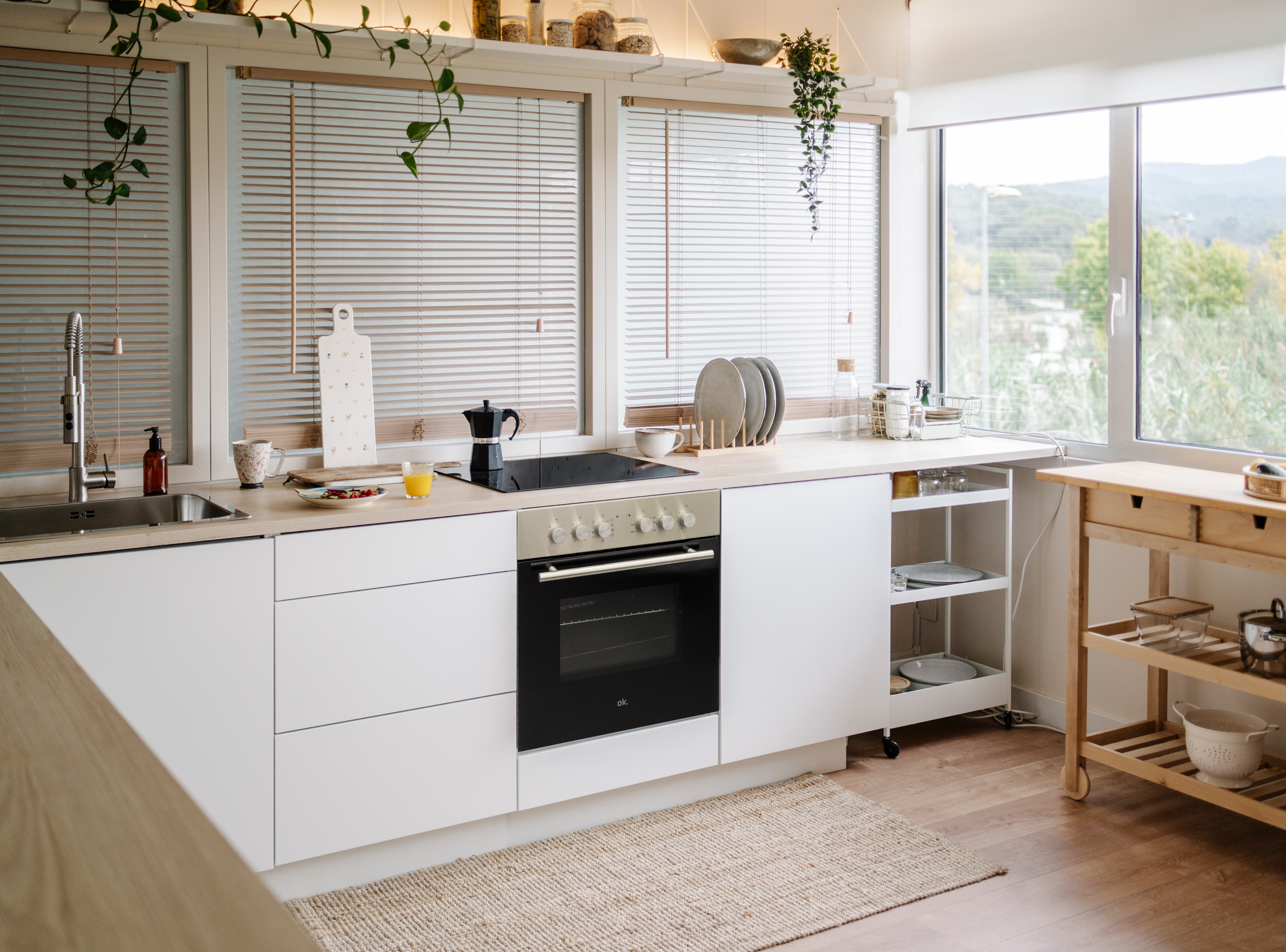 Moderne weiße Küche mit Blick auf üppiges Grün durch große Fenster.