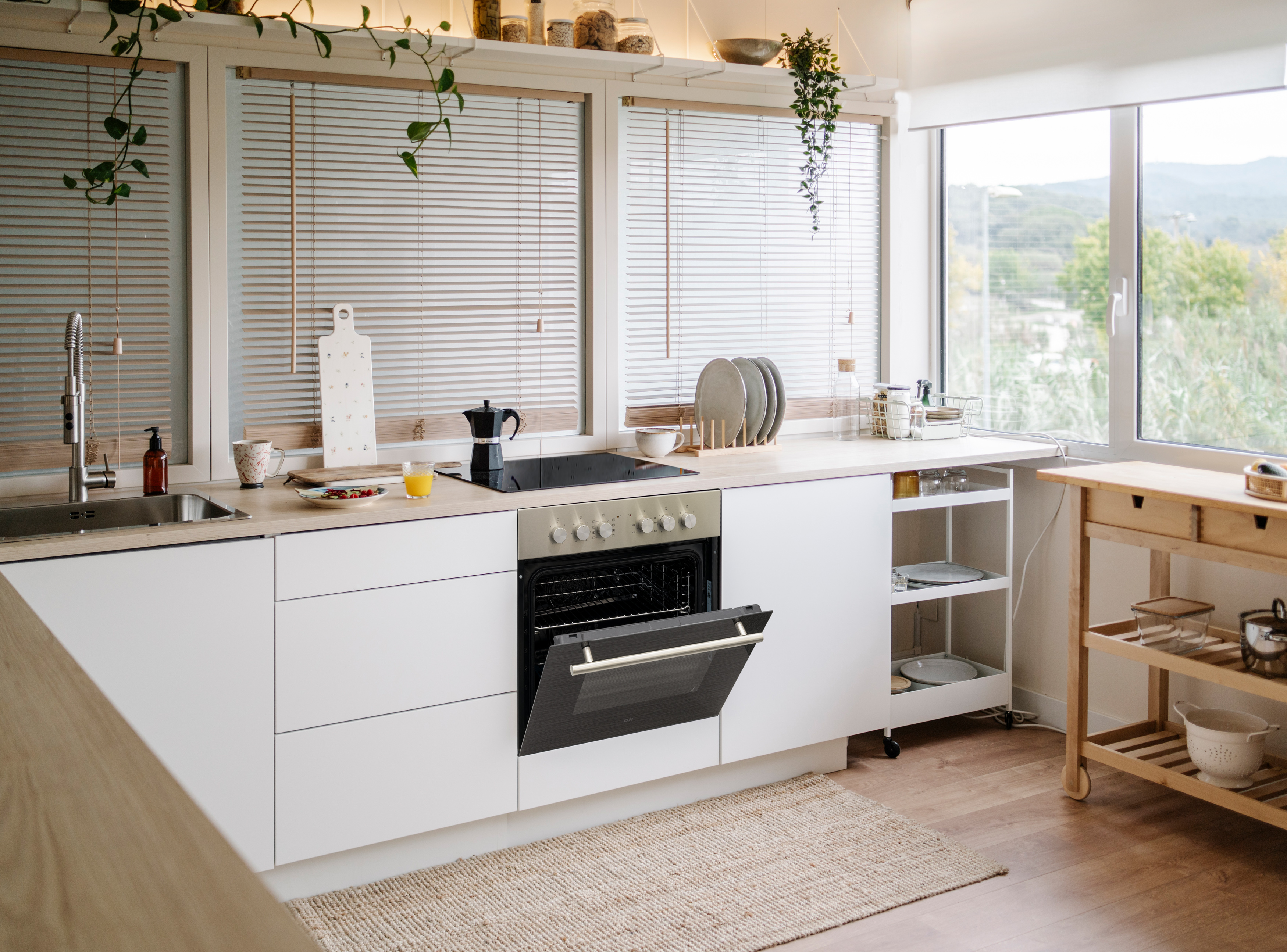 Moderne weiße Küche mit Spüle, Herd und offenem Ofen, Blick nach draußen.