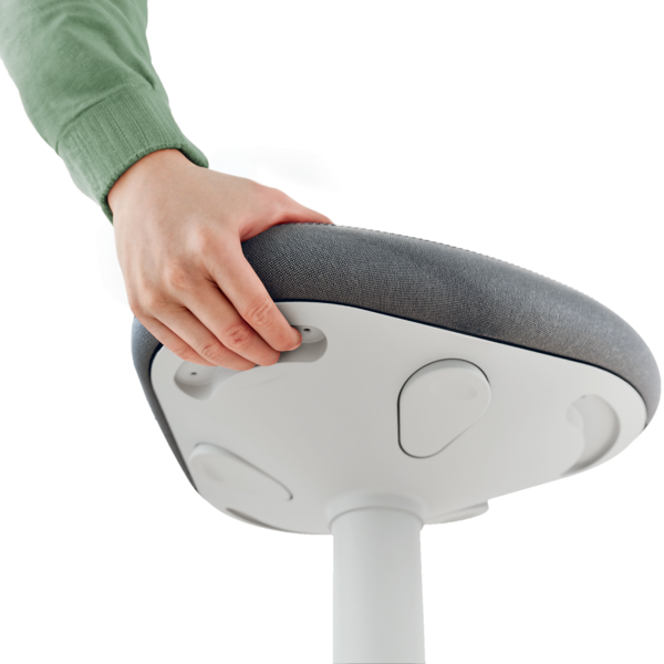 Eine Hand in einem grünen Pullover greift nach einem Hebel am Sitz eines grauen Stuhls.