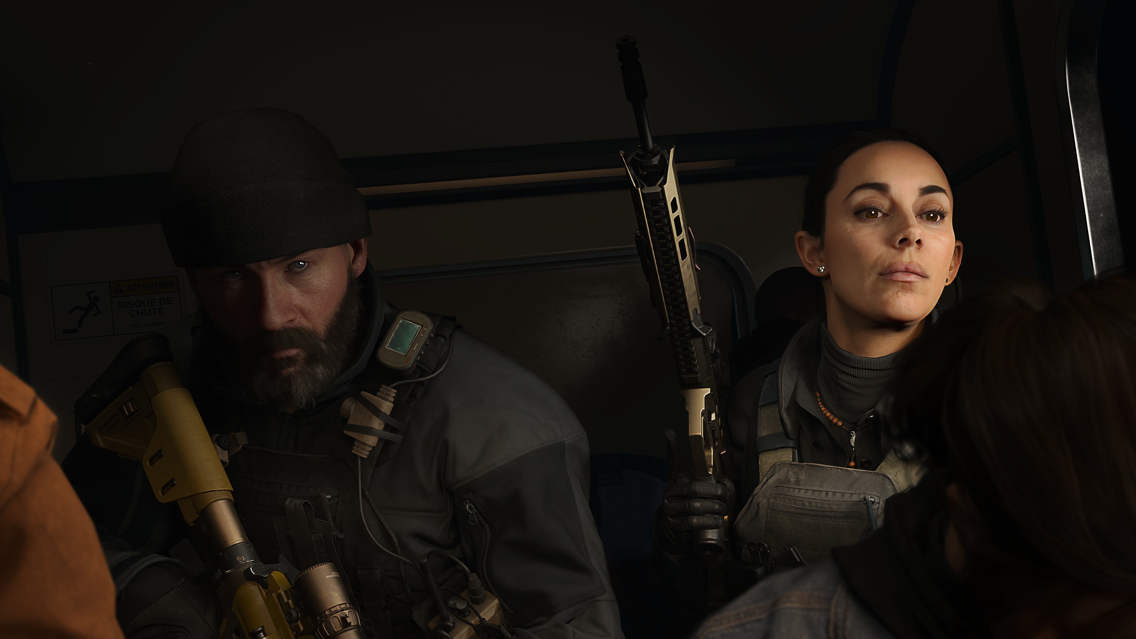 Zwei Soldaten, ein bärtiger Mann, eine Frau, sitzen in einem Fahrzeug und halten Gewehre.