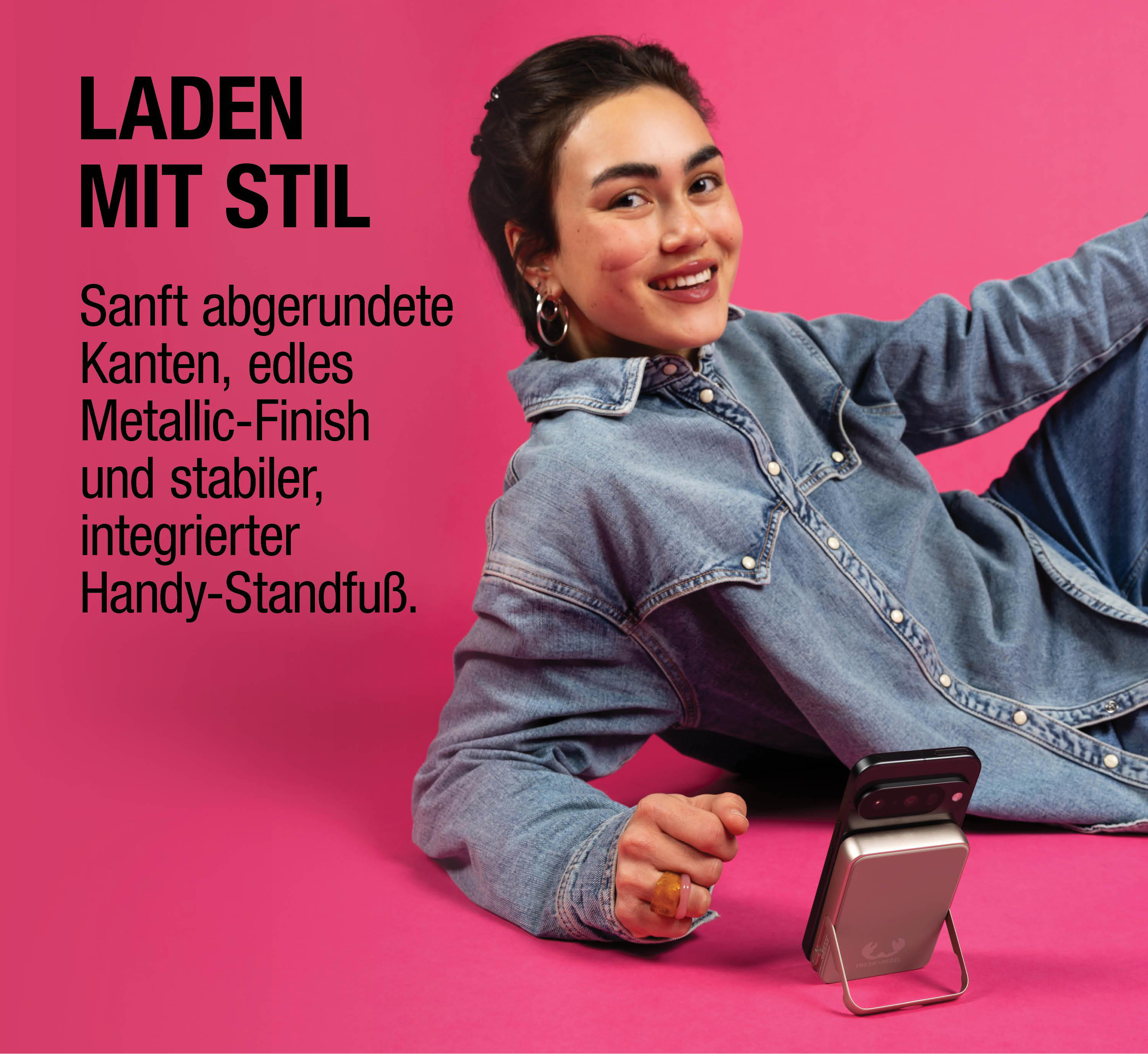 Frau in Jeans lächelt, Handy-Ladegerät steht auf pinkem Hintergrund.