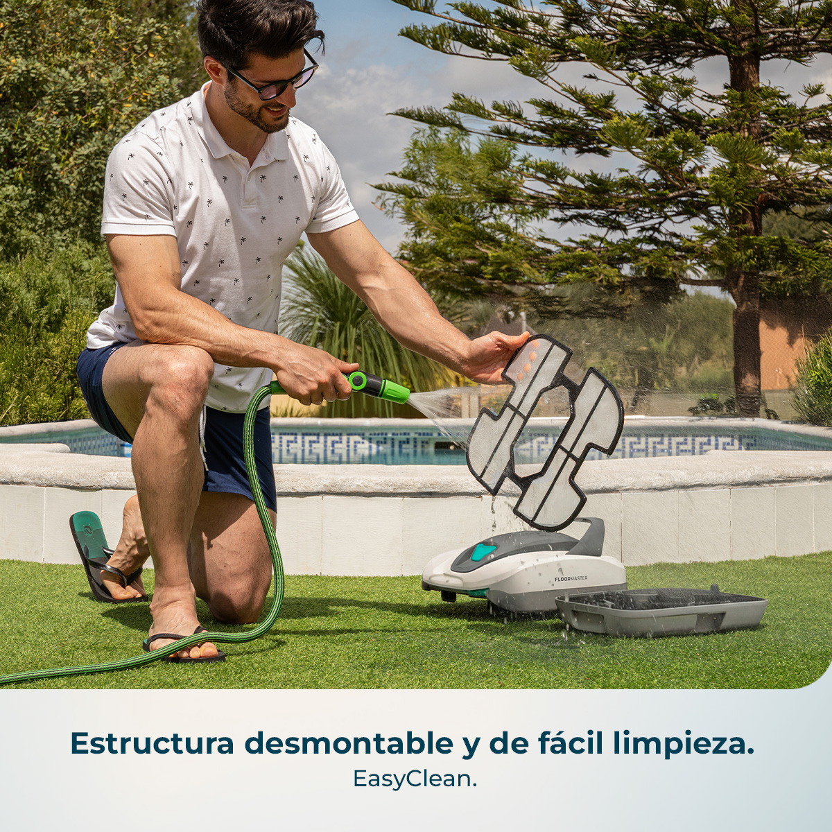 Hombre limpia filtro de robot de piscina con manguera junto a piscina.
