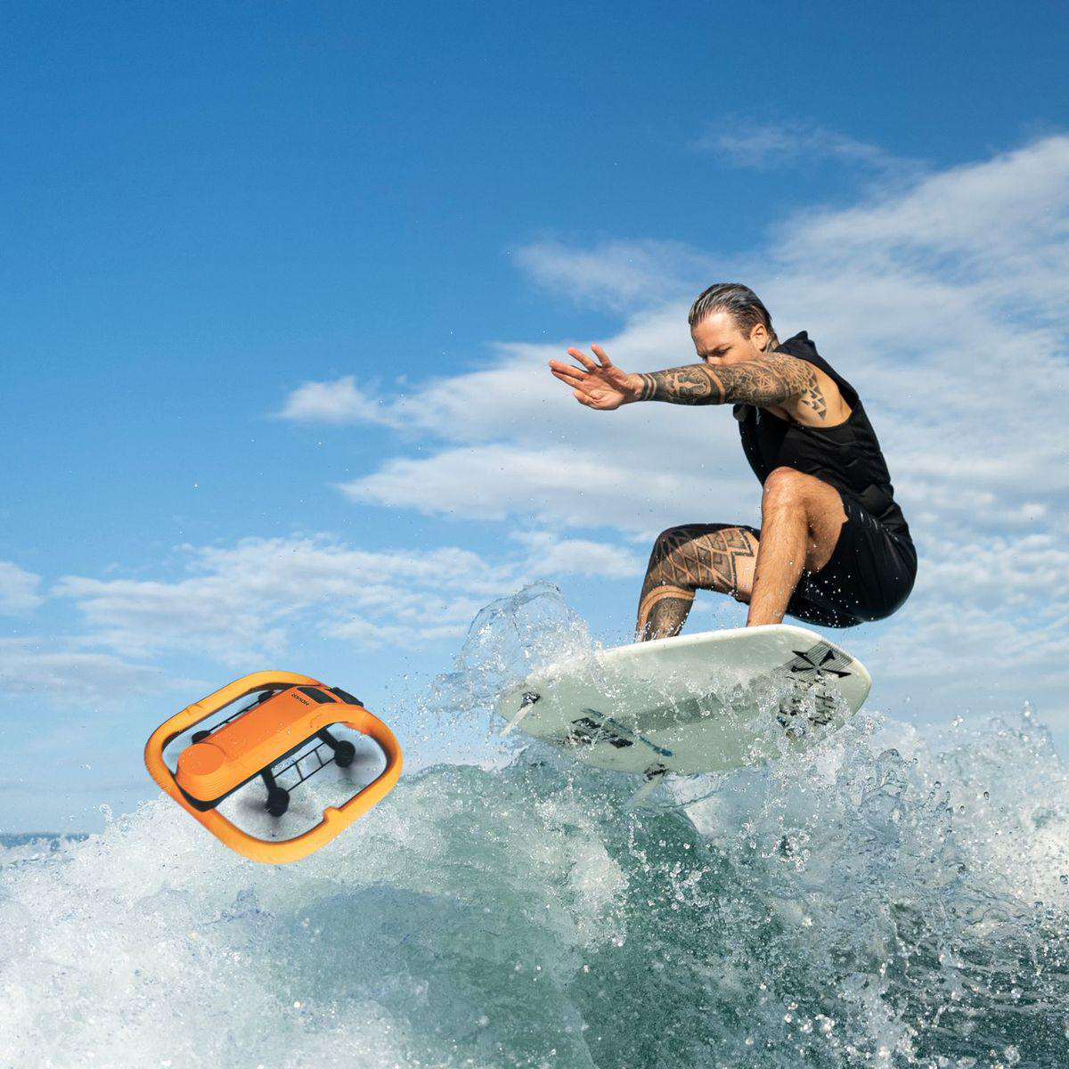 Ein Surfer reitet eine Welle mit einer Drohne in der Nähe unter blauem Himmel.