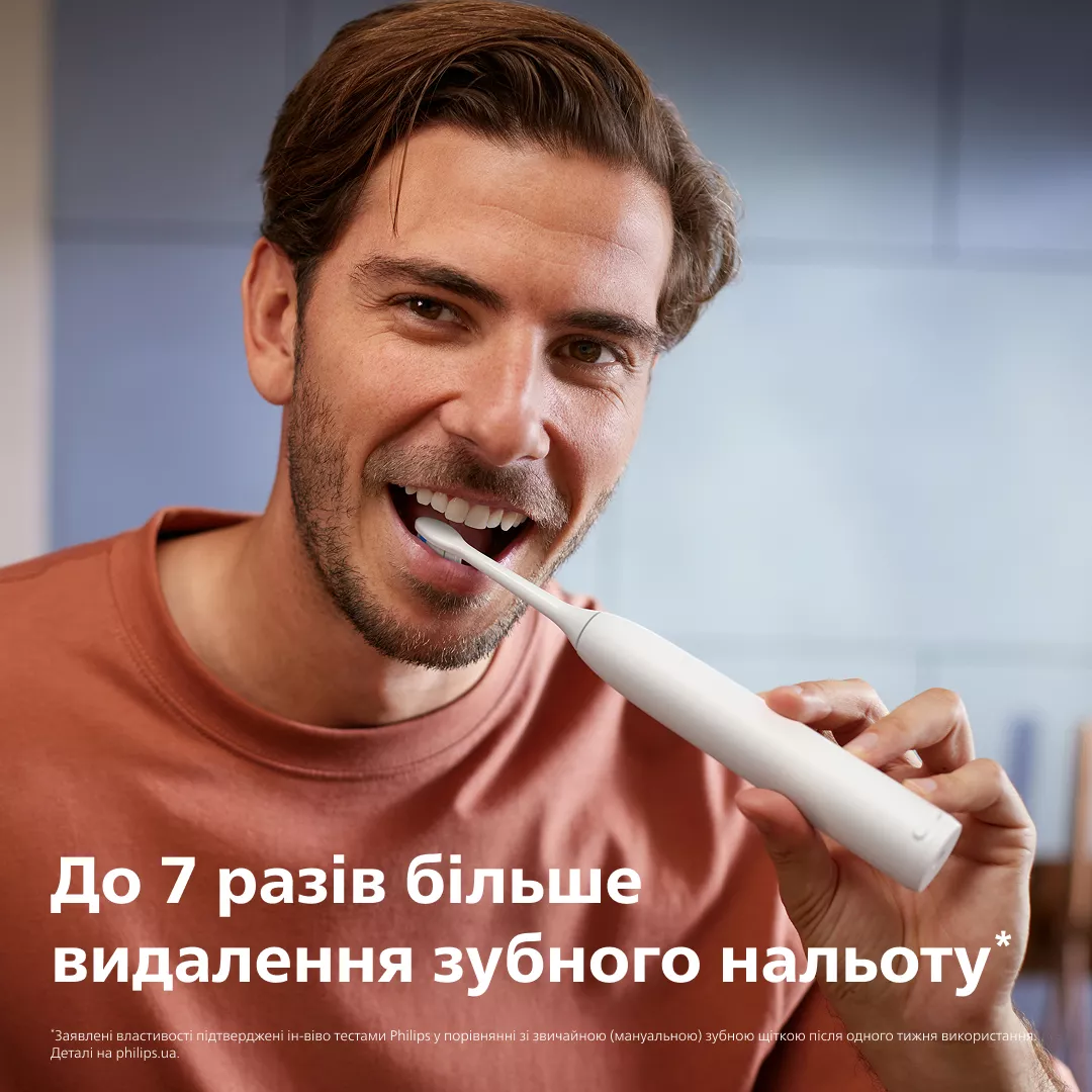 Mężczyzna myje zęby białą szczoteczką elektryczną.