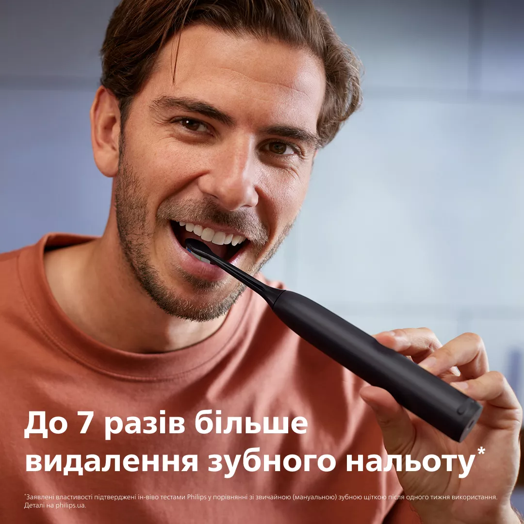 Mężczyzna myje zęby czarną szczoteczką elektryczną.