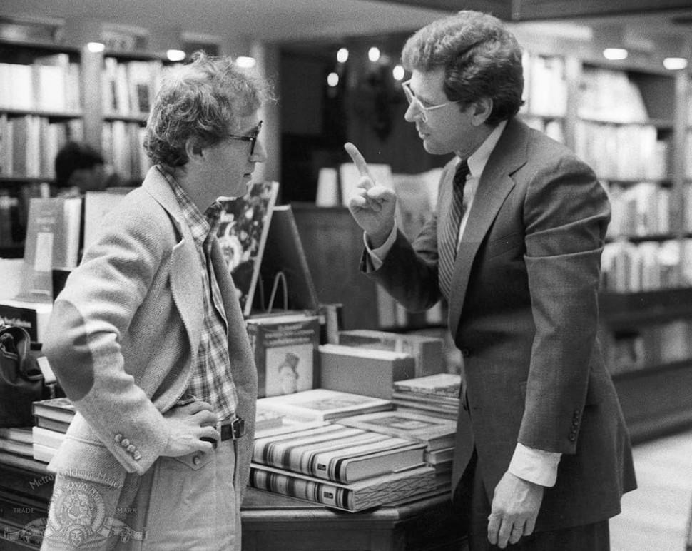Zwei Männer unterhalten sich in einem Buchladen, umgeben von Bücherregalen.