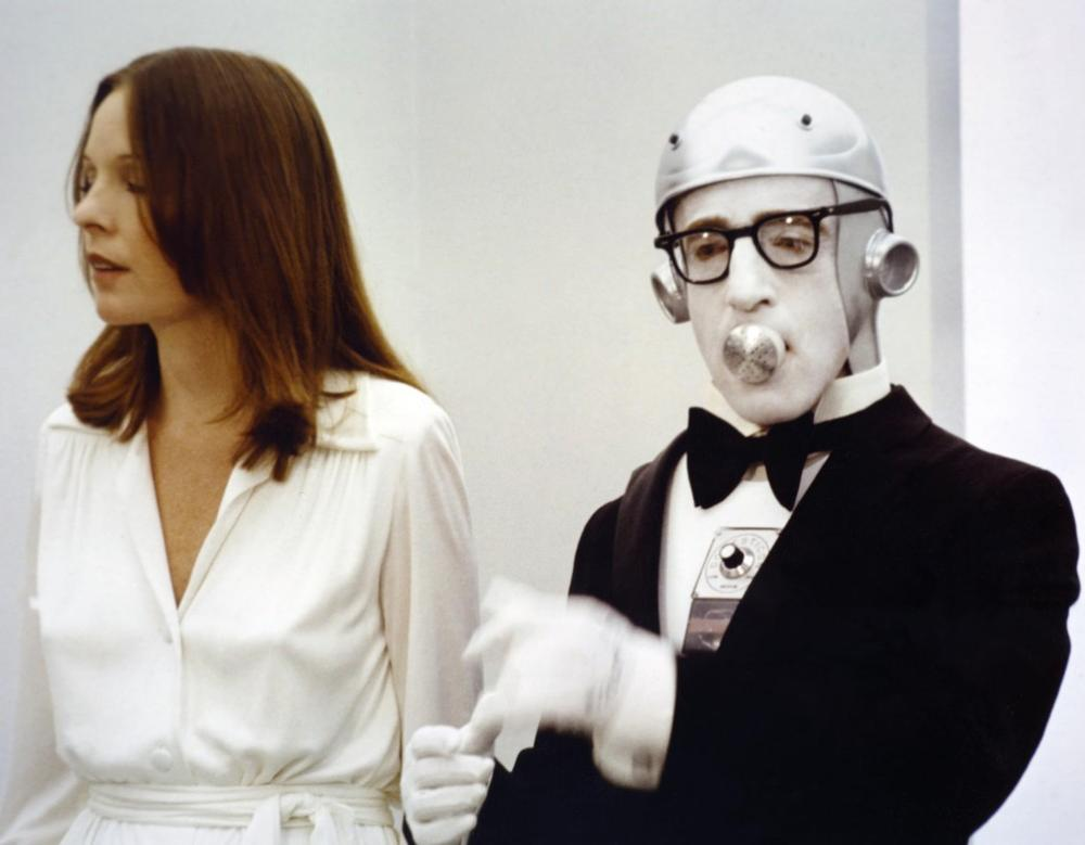 Eine Frau in weiß und ein Mann in einem Roboteranzug mit Brille und Kaubonbon.