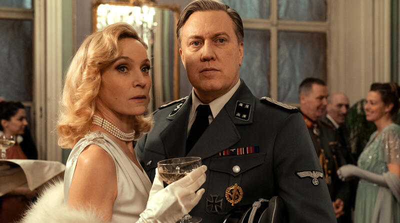 Ein Mann in Uniform und eine Frau in einem Perlenkleid posieren.