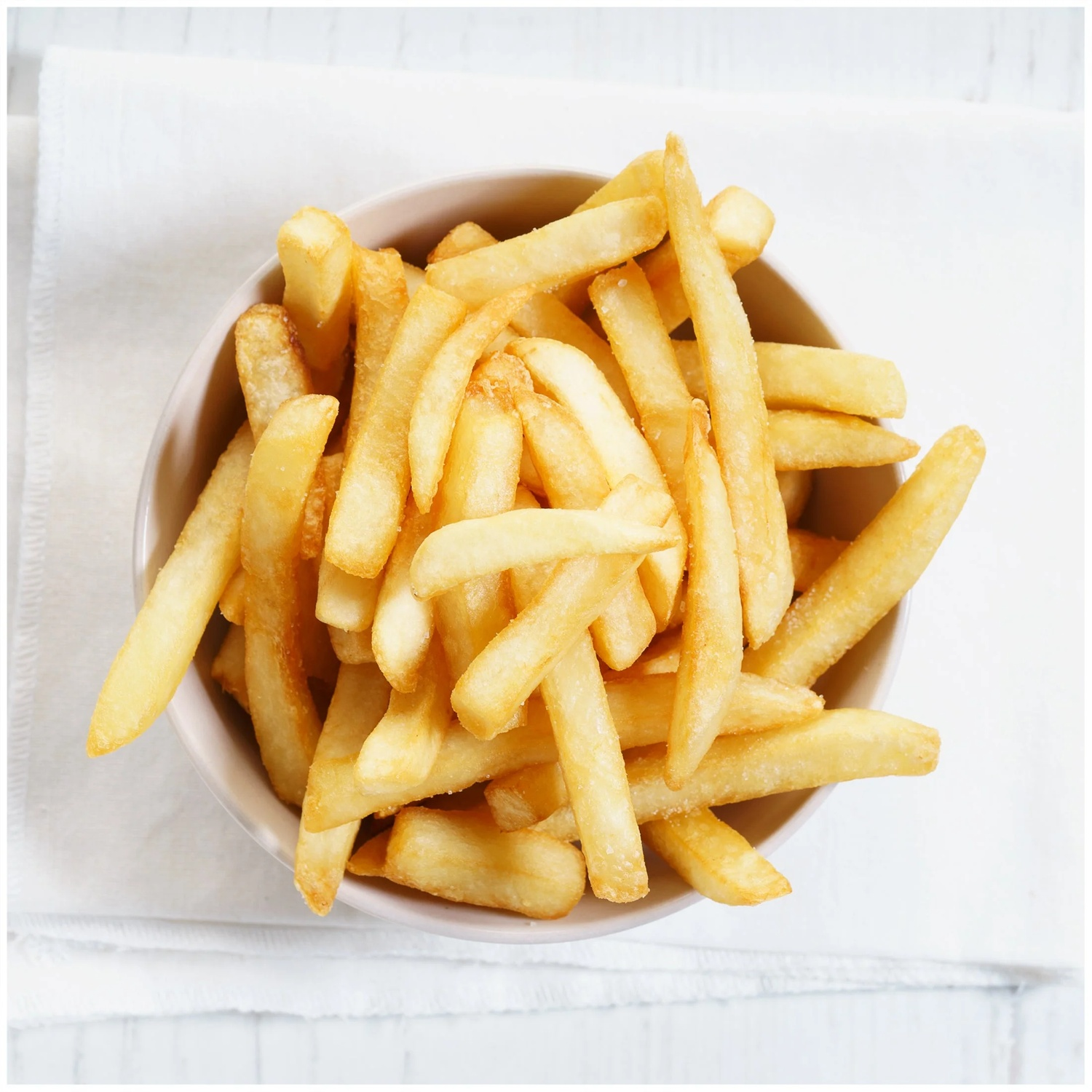 Un bol rempli de frites dorées et croustillantes sur un tissu blanc.