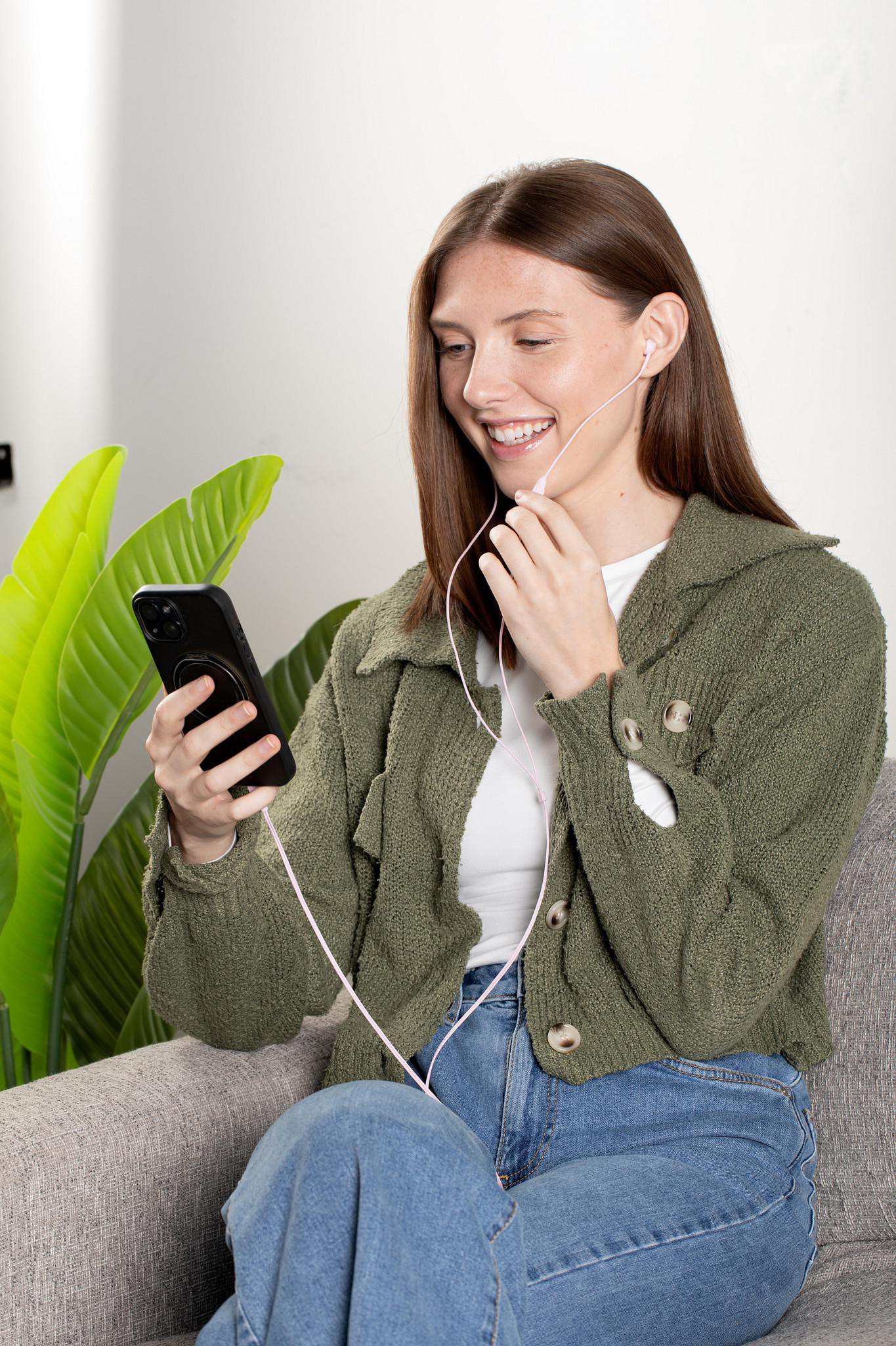 Eine Frau mit Kopfhörern und Handy auf einem Sofa.